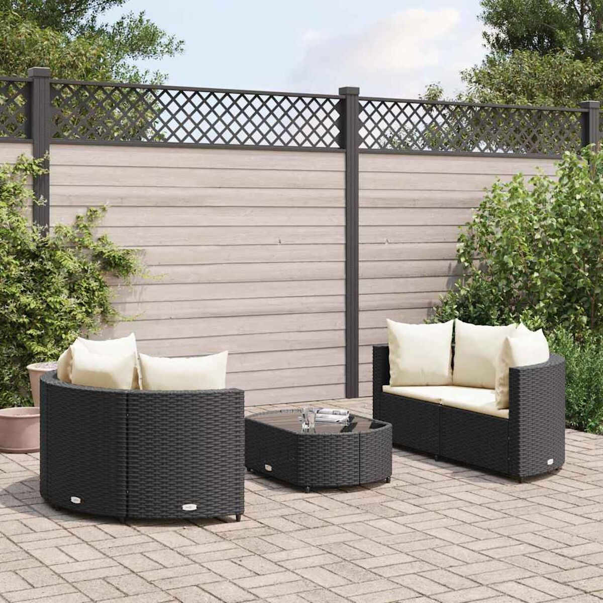 Set divano da esterno in vimini nero, con tavolo, su un patio, con cuscini beige e una recinzione dietro.