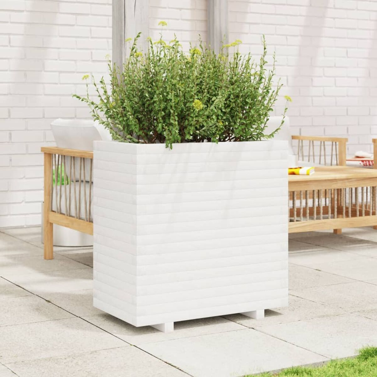 Weißer quadratischer Pflanzkübel mit grüner Pflanze und gelben Blüten auf einer Terrasse.