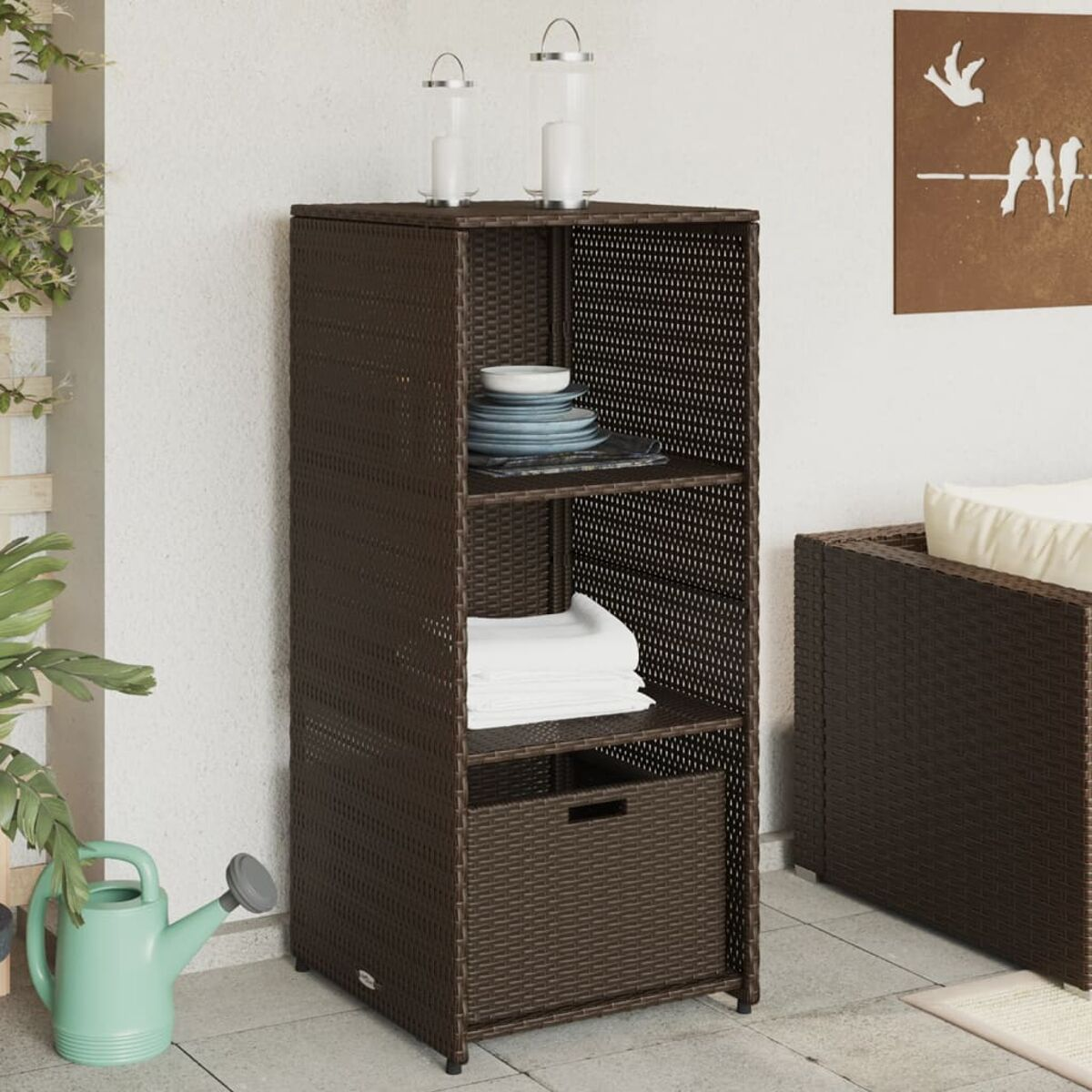 Ein brauner Rattan-Aufbewahrungsschrank mit Regalen und einer Schublade. Geschirr, Handtücher und Dekor sind auf den Regalen.
