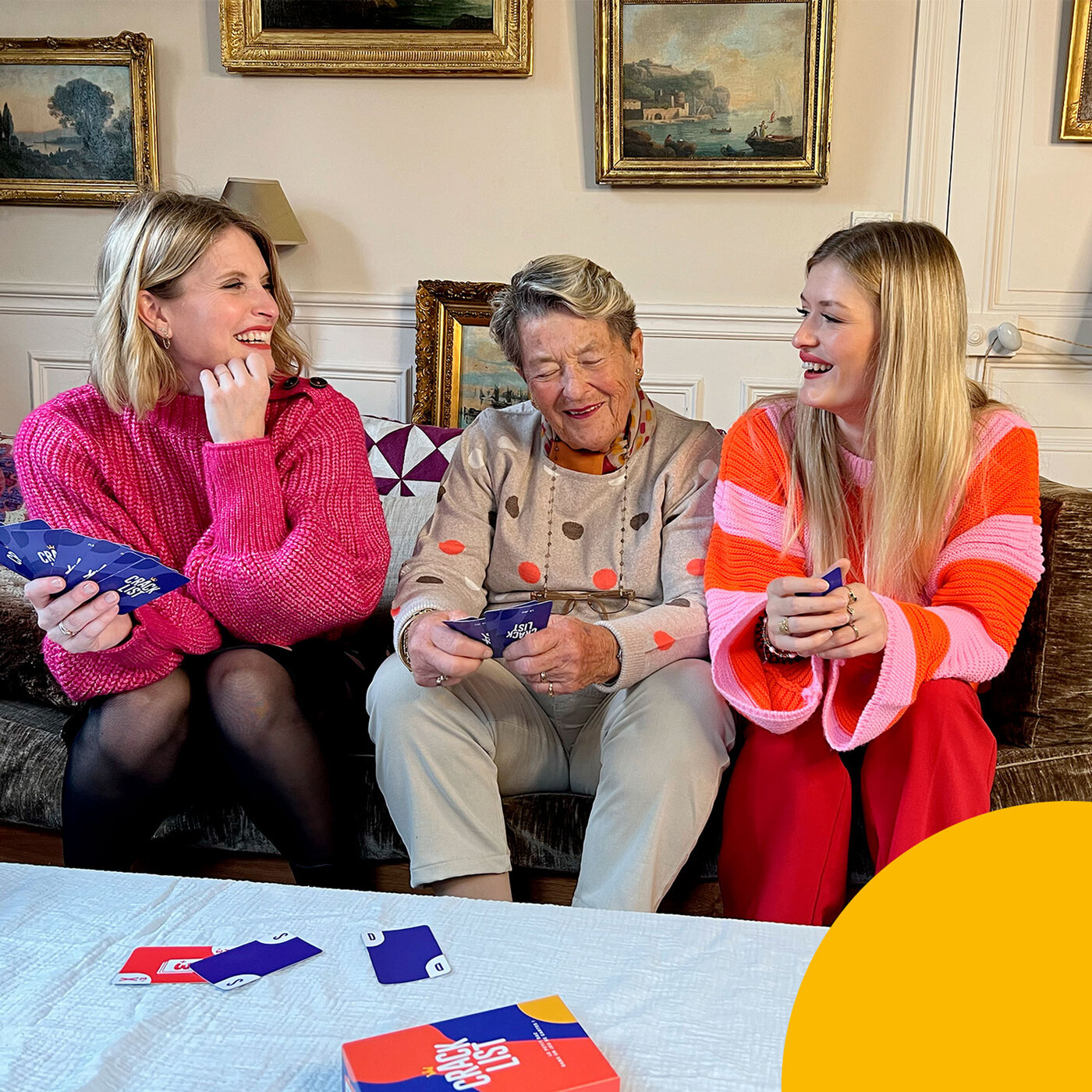 Trois femmes jouent à un jeu de cartes. Elles sourient et rient.