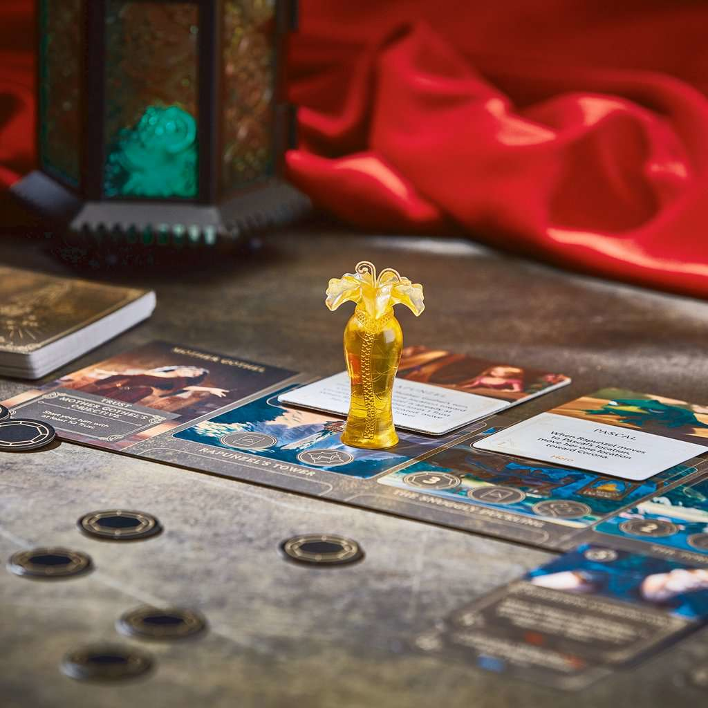 Gra planszowa z kartami i pionkami. Złota figurka sukienki stoi na kartach. Czerwona tkanina w tle.