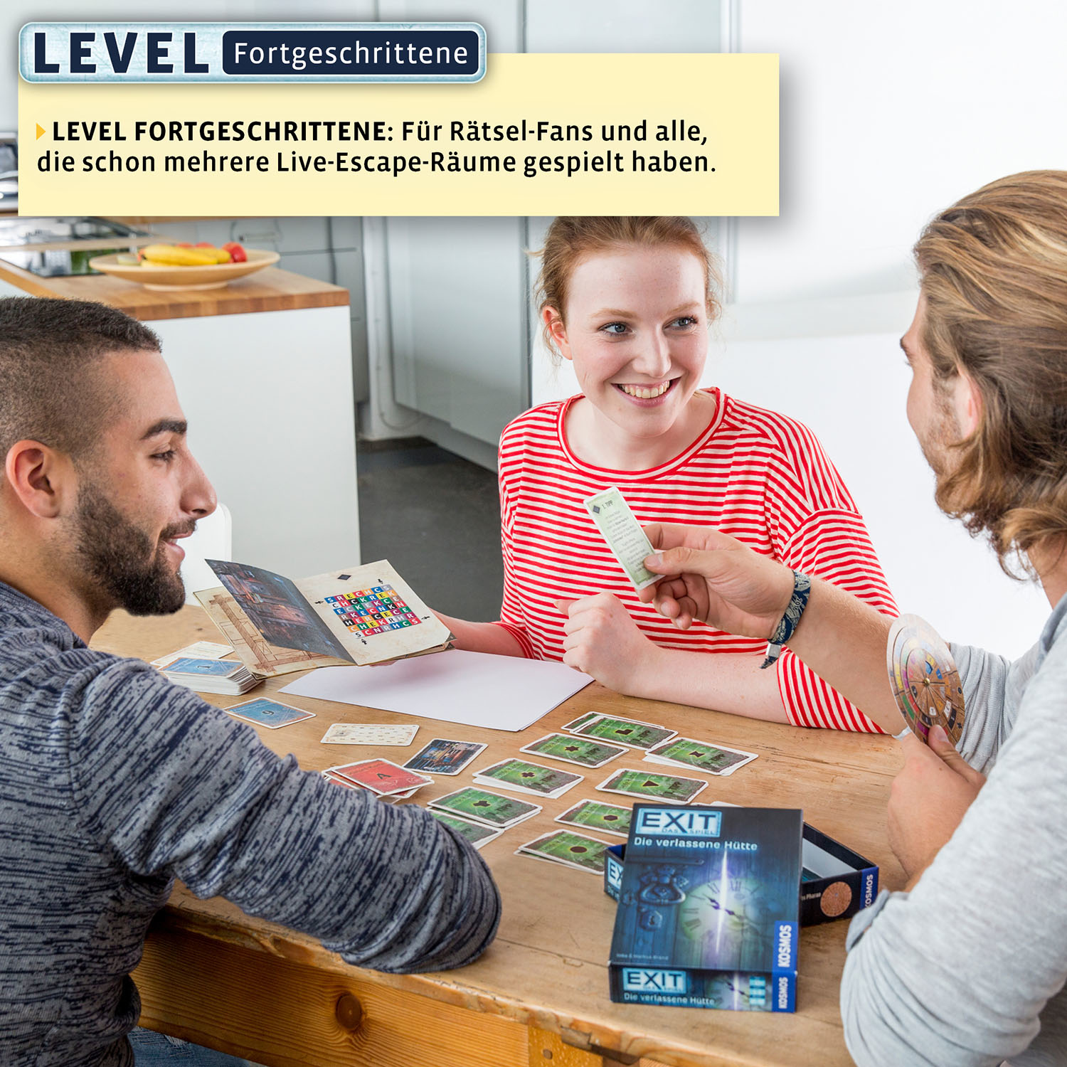 Drei Personen spielen ein Brettspiel mit Karten und einer Spielbox auf einem Holztisch.
