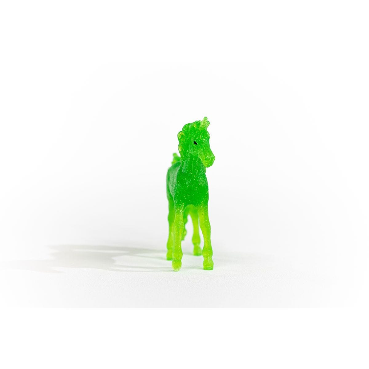 Eine kleine, grüne, durchscheinende Plastik-Einhornfigur steht auf einer weißen Oberfläche.