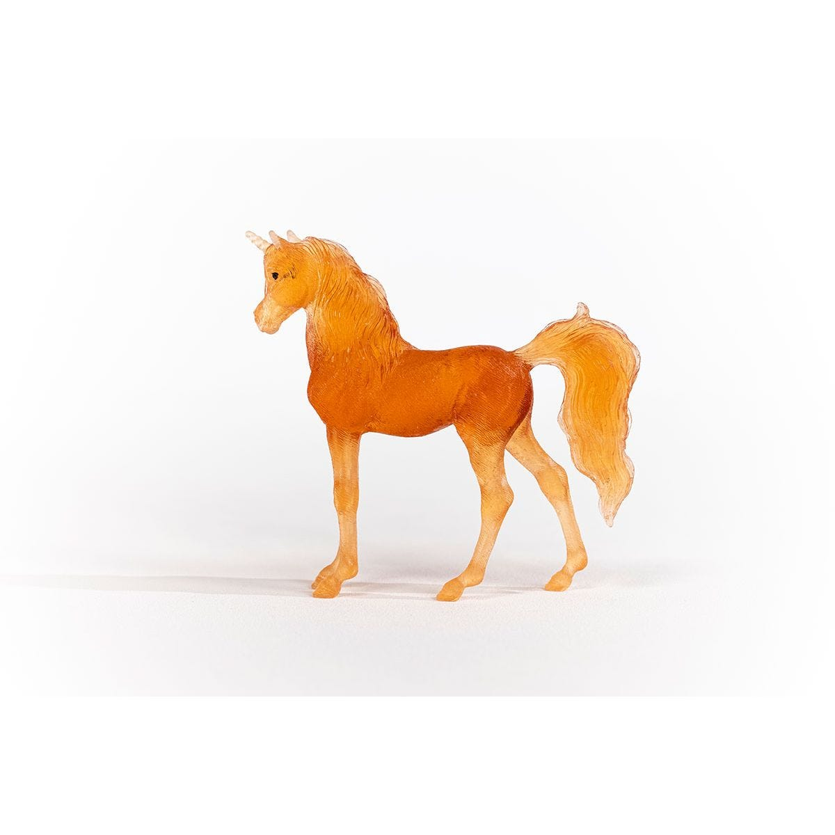 Ein Spielzeugpferd steht auf weißem Untergrund. Es ist ein orangefarbenes Einhorn-Spielzeug mit fließendem Schweif und Mähne.