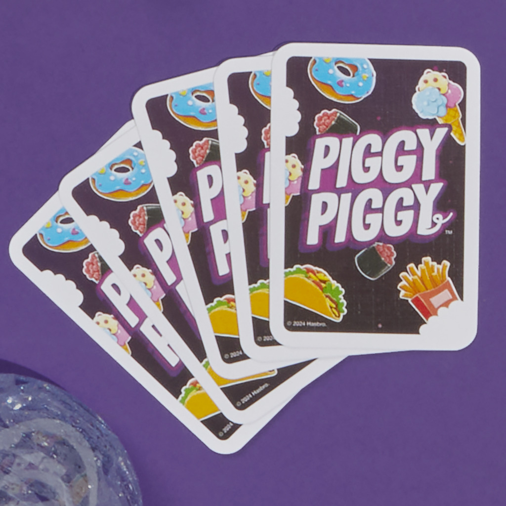 Vier Piggy Piggy-Spielkarten, jede mit Essensillustrationen, auf einer lila Oberfläche.