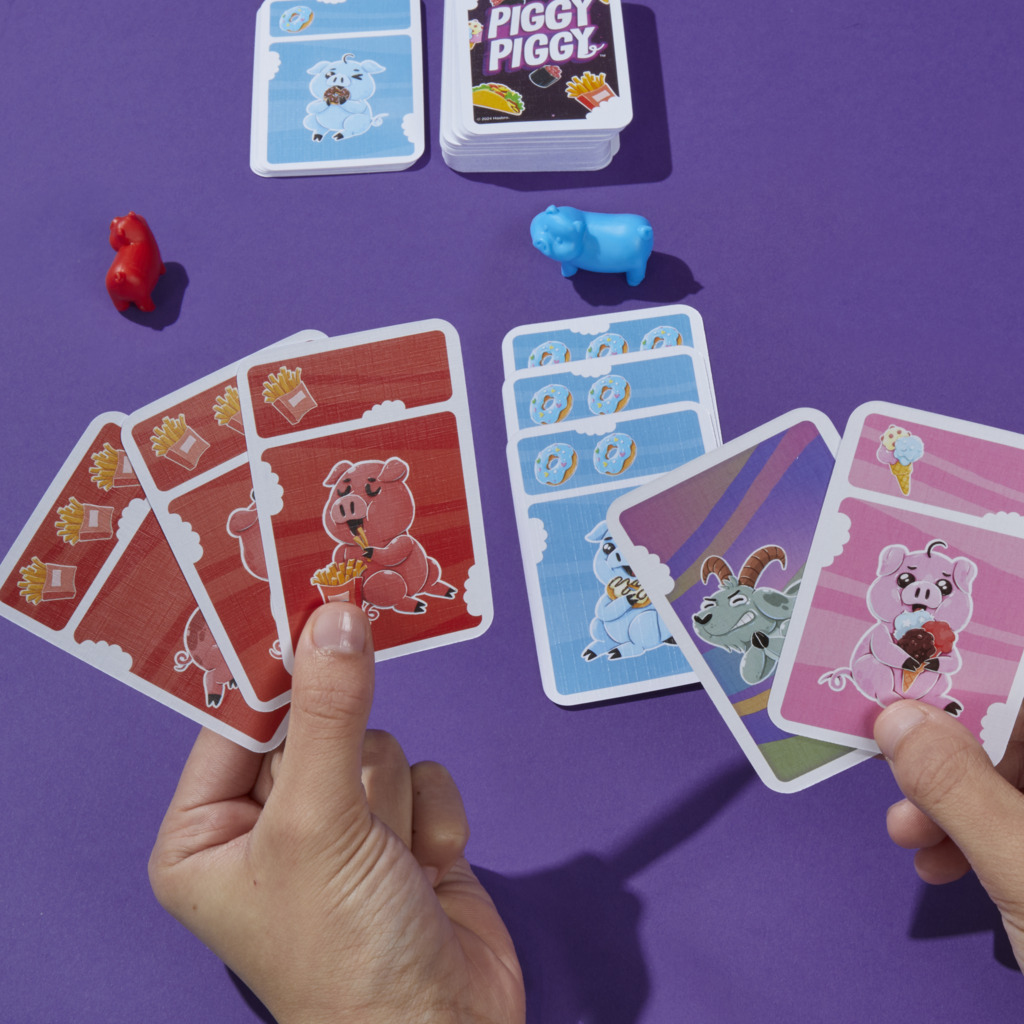 Hände spielen ein Kartenspiel mit verschiedenen Karten zum Thema Schwein auf lila Hintergrund.