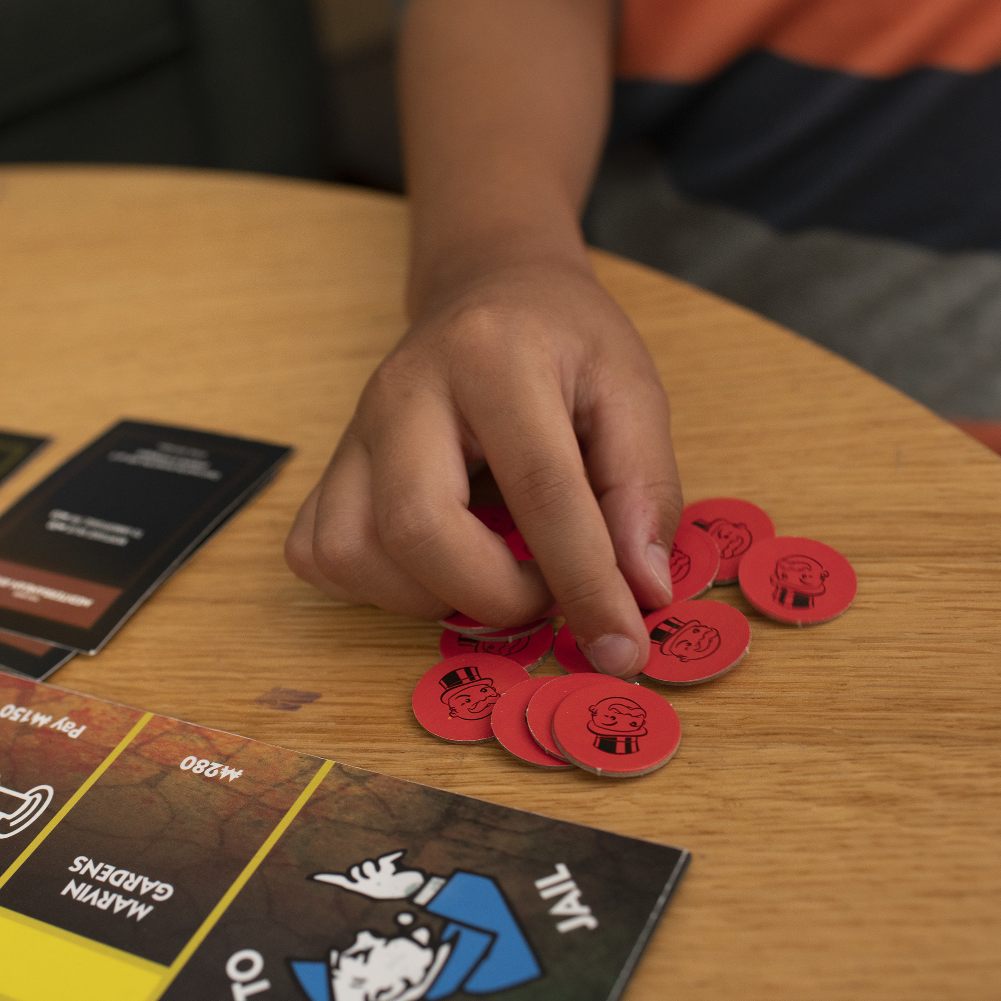 Hand greift nach roten Spielmarken im Monopoly-Spiel auf einem Holztisch.