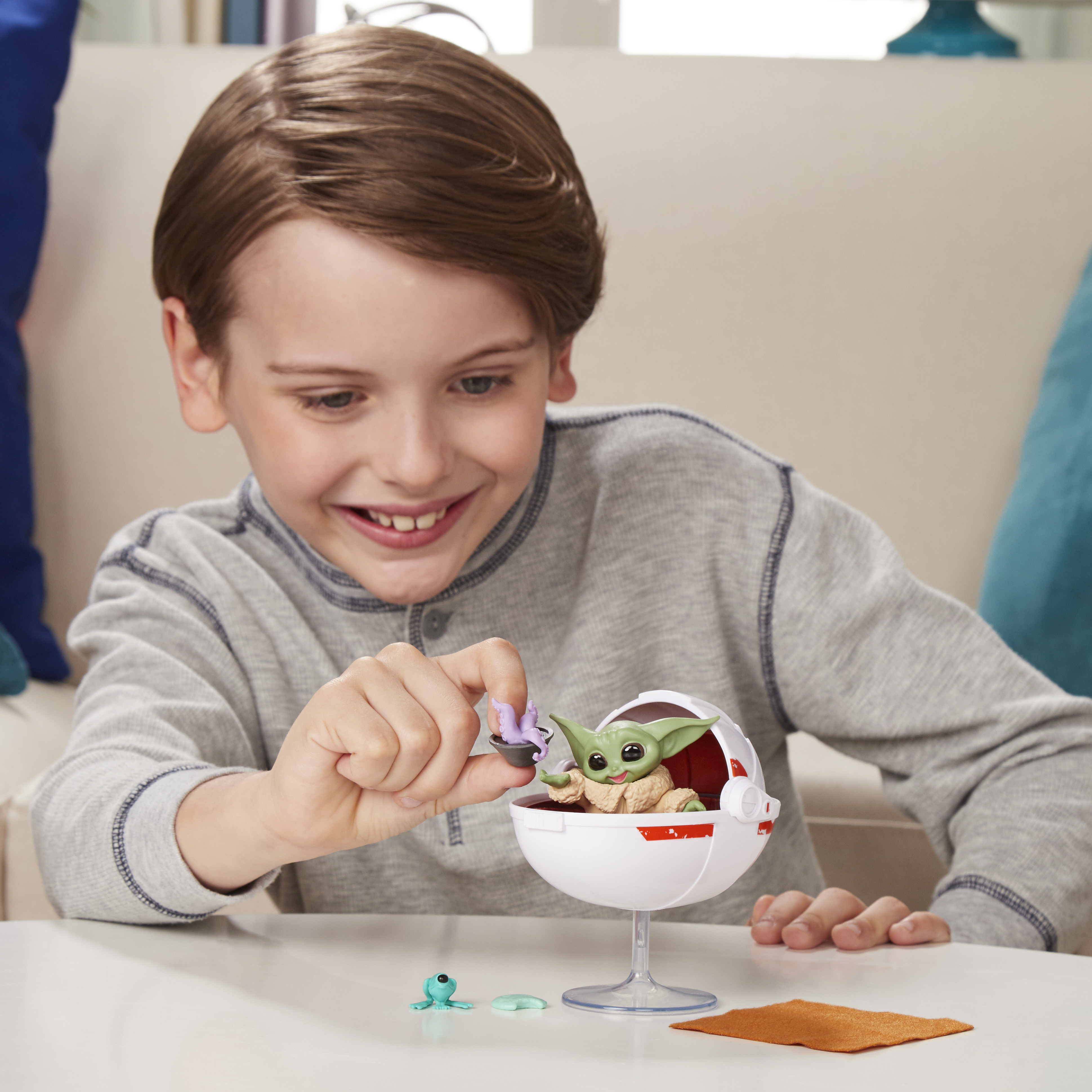 Un bambino sorride mentre gioca con un giocattolo, una figura di Baby Yoda in una capsula bianca.