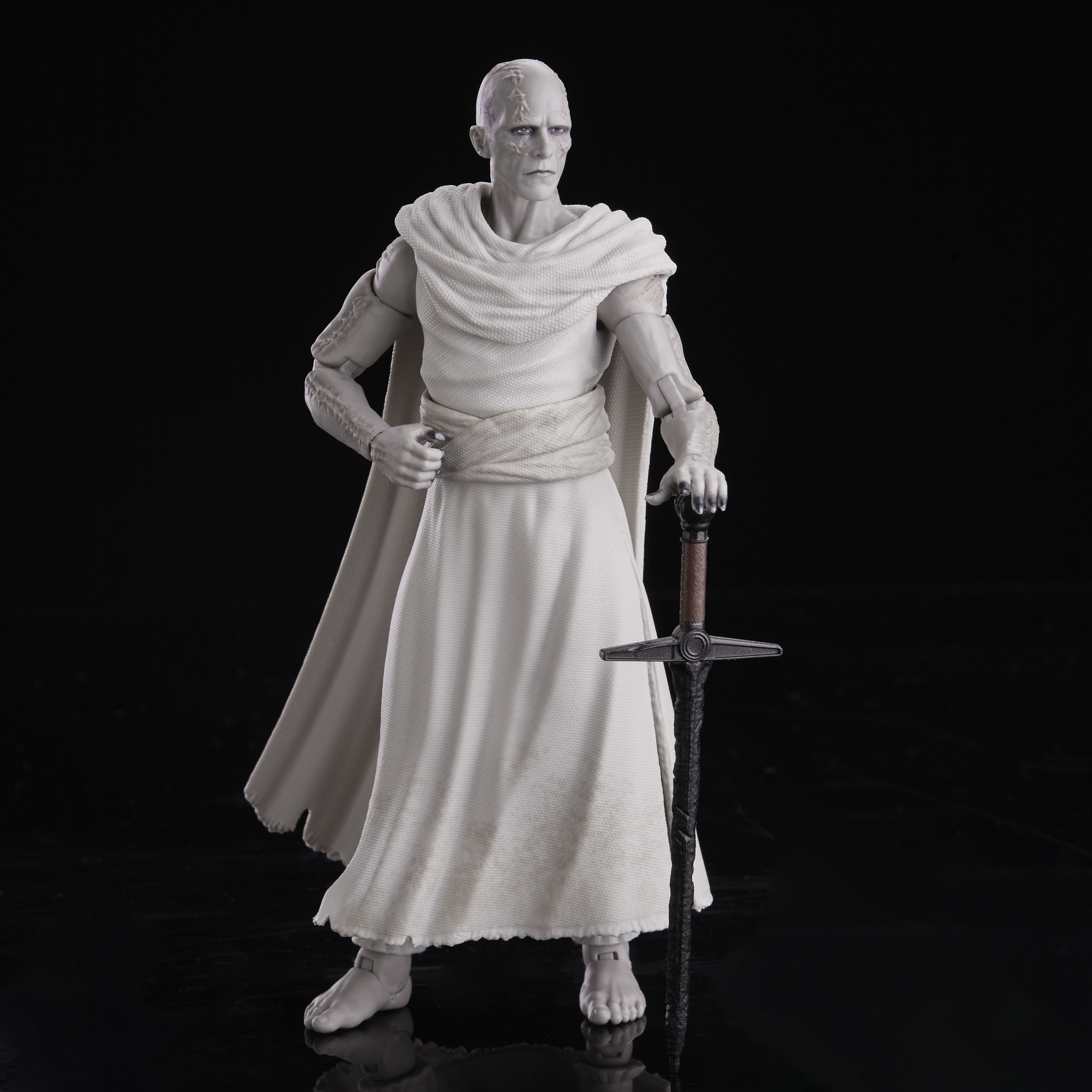 Figurka Gorra trzymająca miecz, w białym stroju, stojąca na czarnej powierzchni.