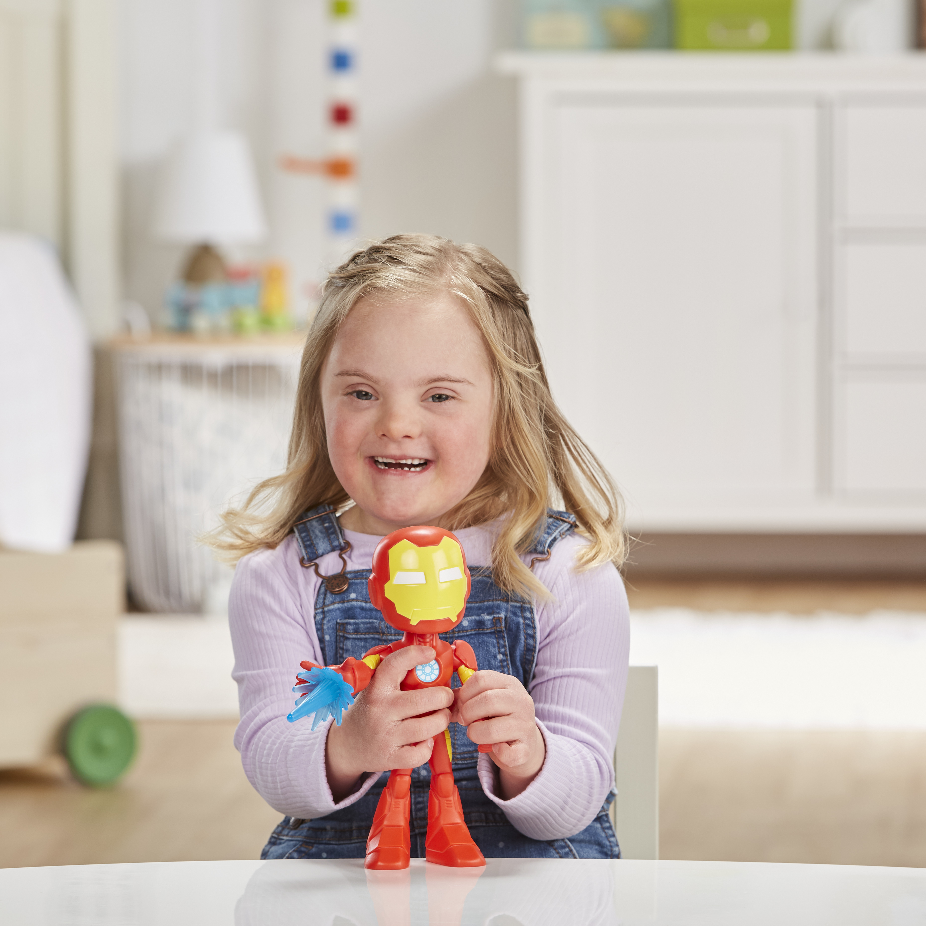 Una bambina tiene in mano un giocattolo di Iron Man. Sorride, indossando una salopette di jeans.