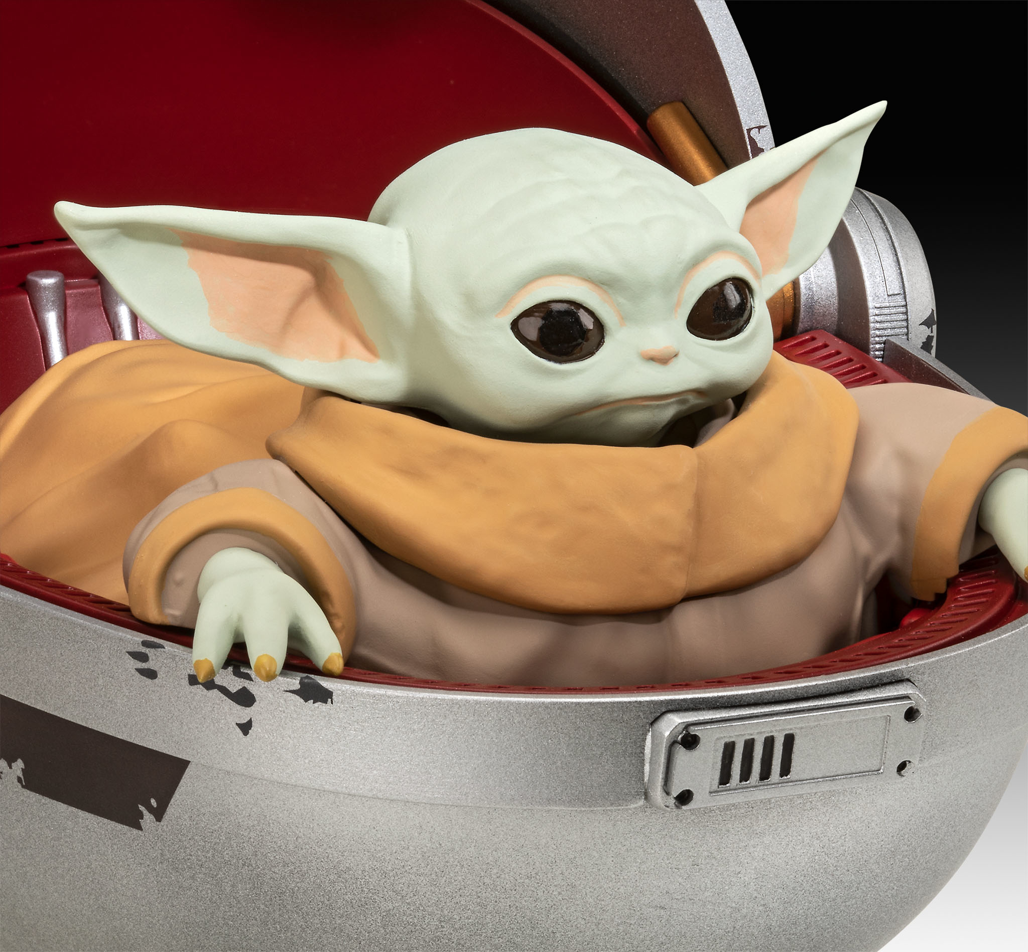 Baby Yoda in a pod. The pod is red and silver. Baby Yoda has big eyes.