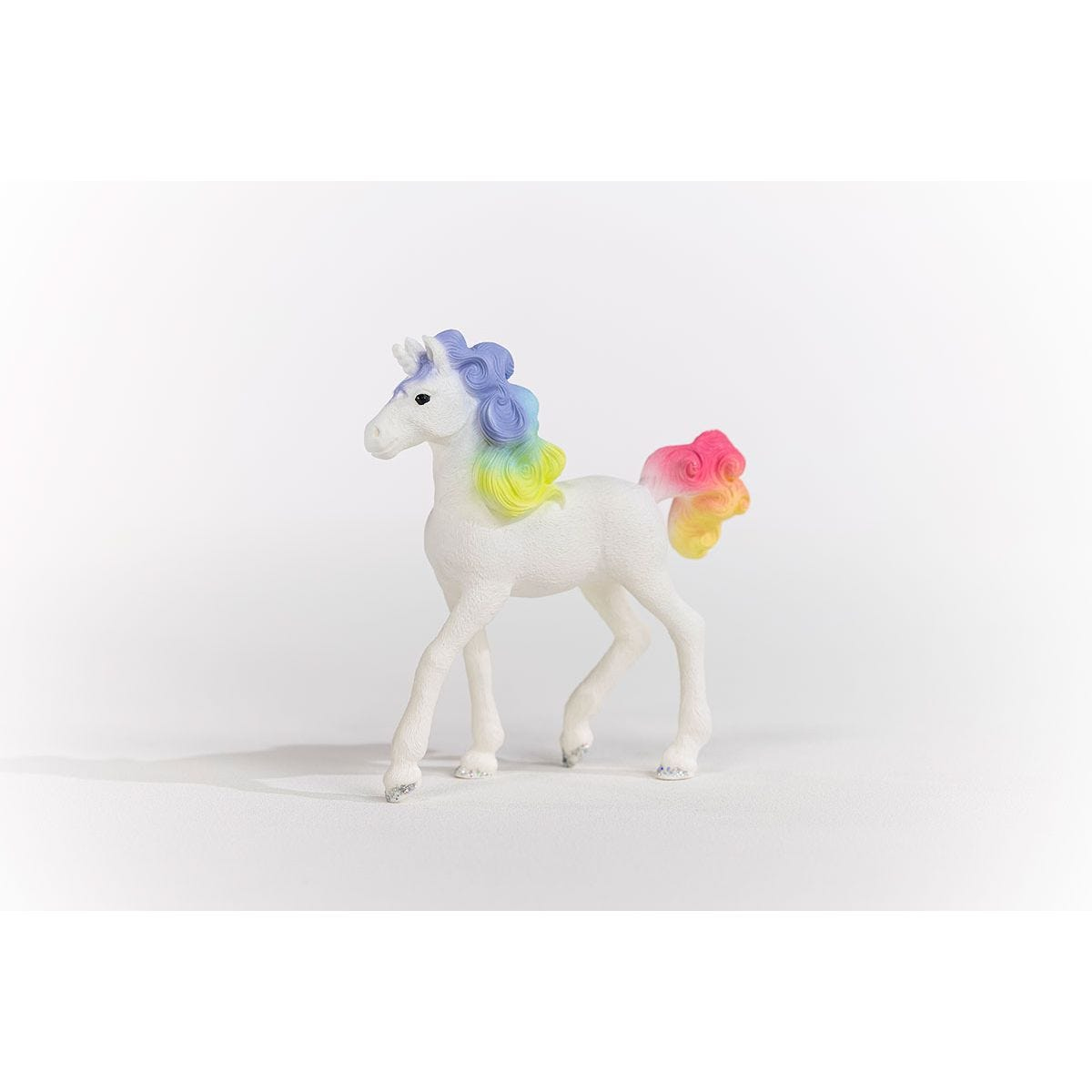 Biały zabawkowy jednorożec z tęczową grzywą i ogonem. Na białej powierzchni, na białym tle.