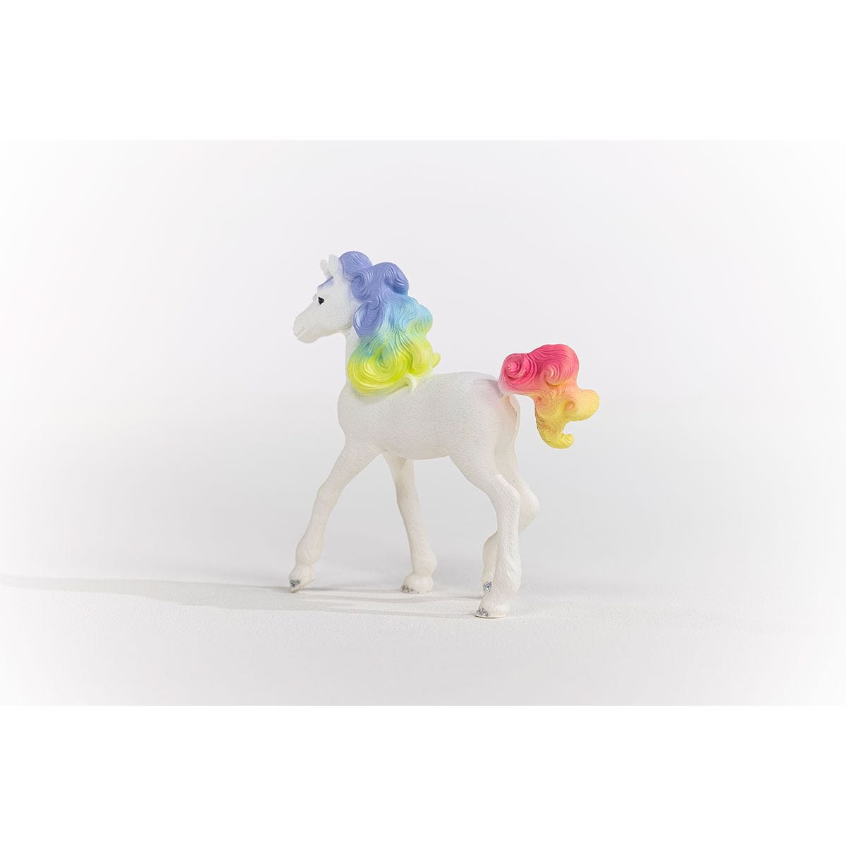 Zabawkowy koń z tęczową grzywą i ogonem. Stoi na białej powierzchni.