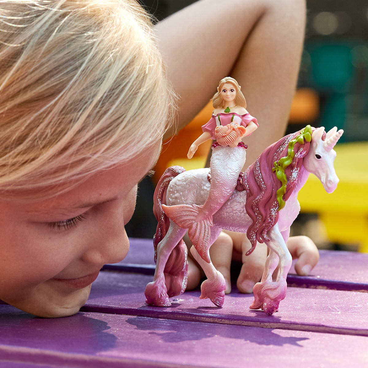 Ein junges Mädchen betrachtet eine Meerjungfrau-Figur, die auf einem Einhorn auf einem lila Tisch reitet.