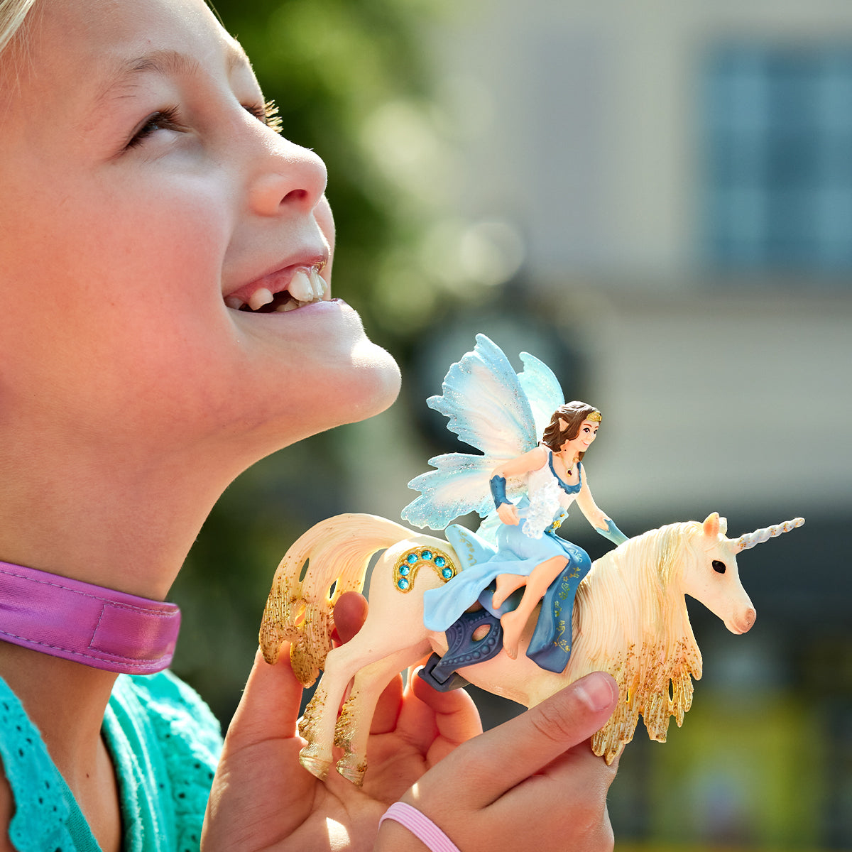 Ein junges Mädchen lächelt und hält ein Spielzeug-Einhorn mit einer Fee darauf. Verschwommener Hintergrund.