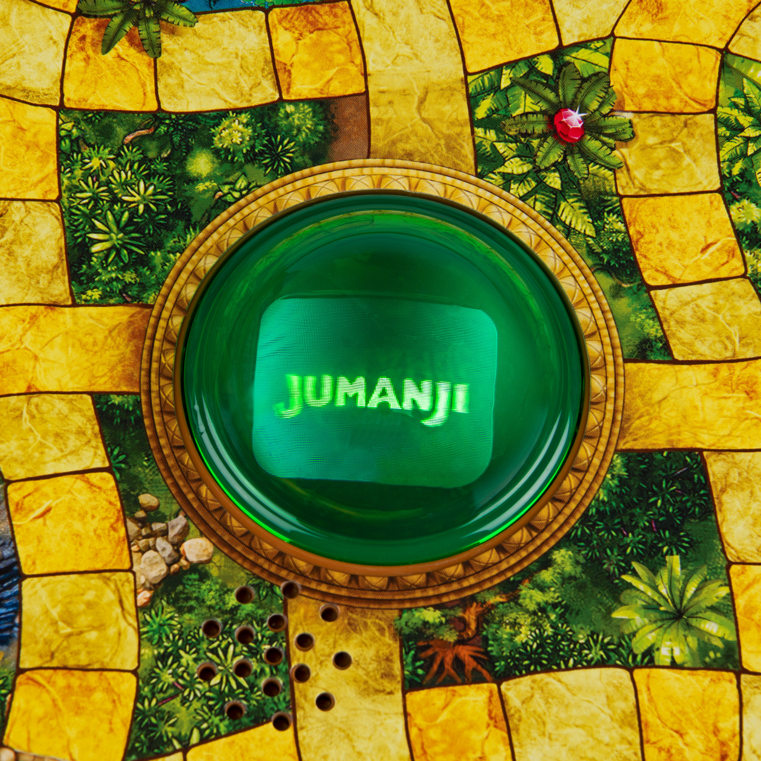 Draufsicht auf den zentralen, grün beleuchteten Knopf eines Jumanji-Brettspiels innerhalb des Spielbretts.