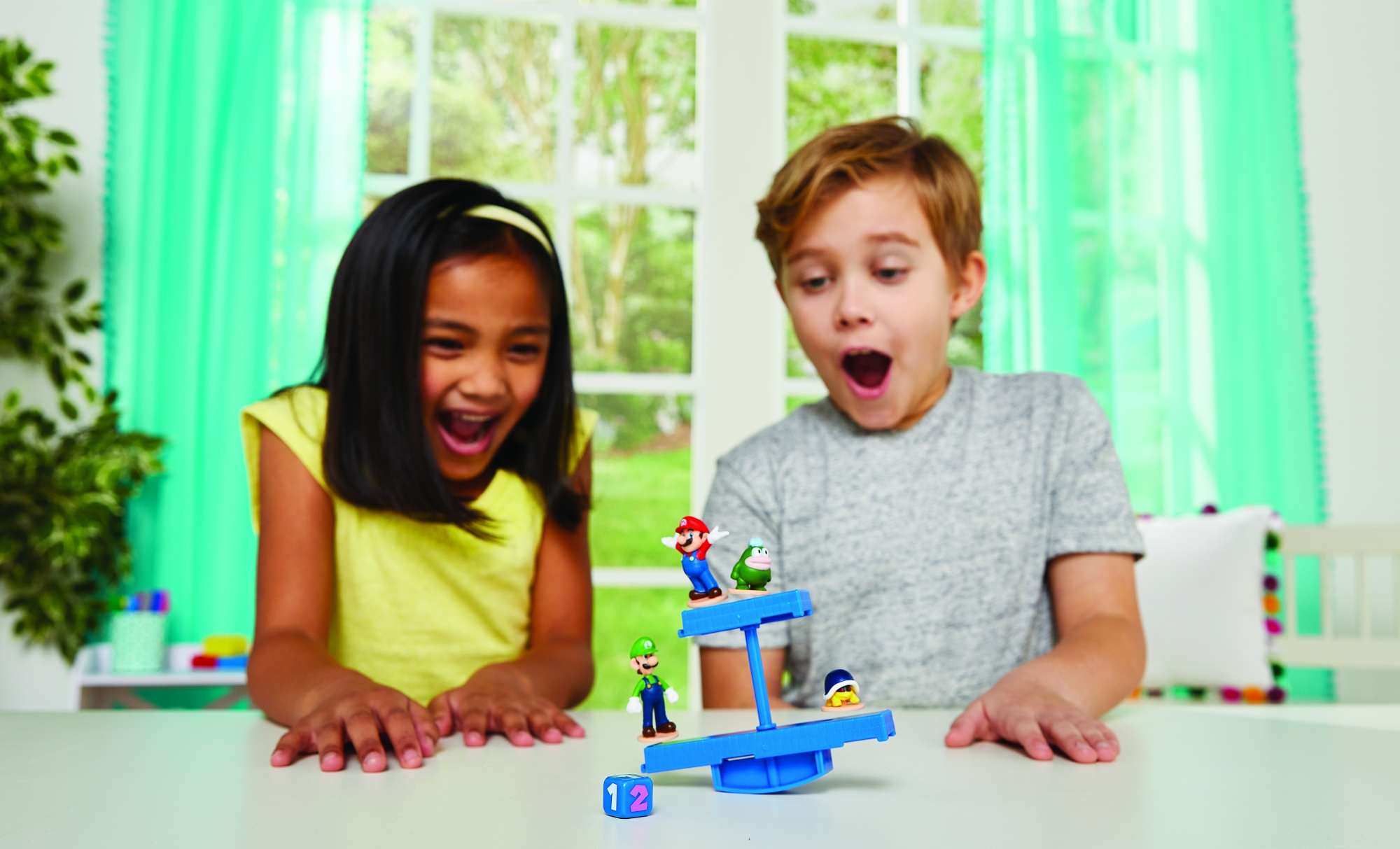 Dwoje dzieci, dziewczynka i chłopiec, patrzą na zabawkę równoważną z małymi figurkami.