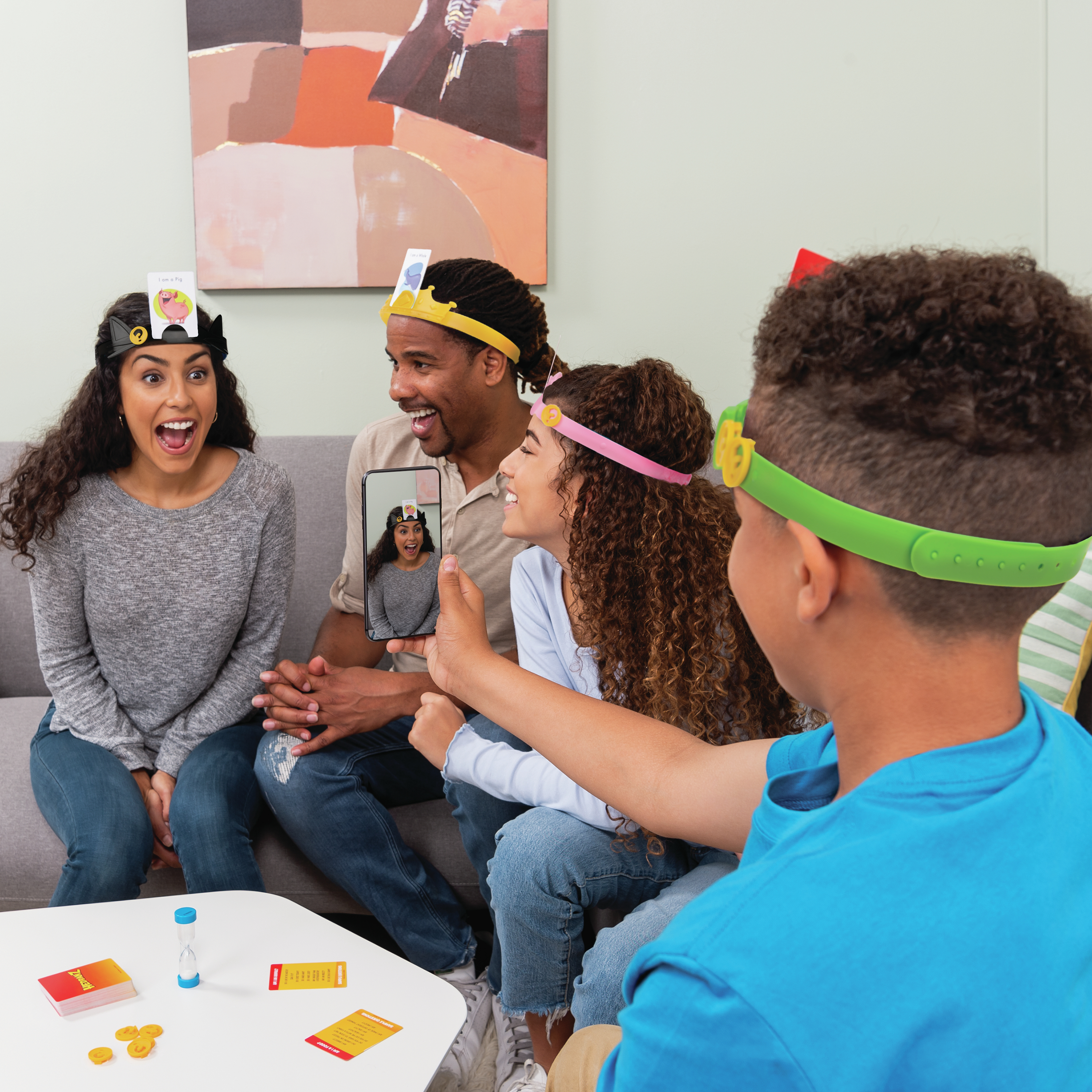 Familie spielt ein Brettspiel, trägt Stirnbänder mit Karten.