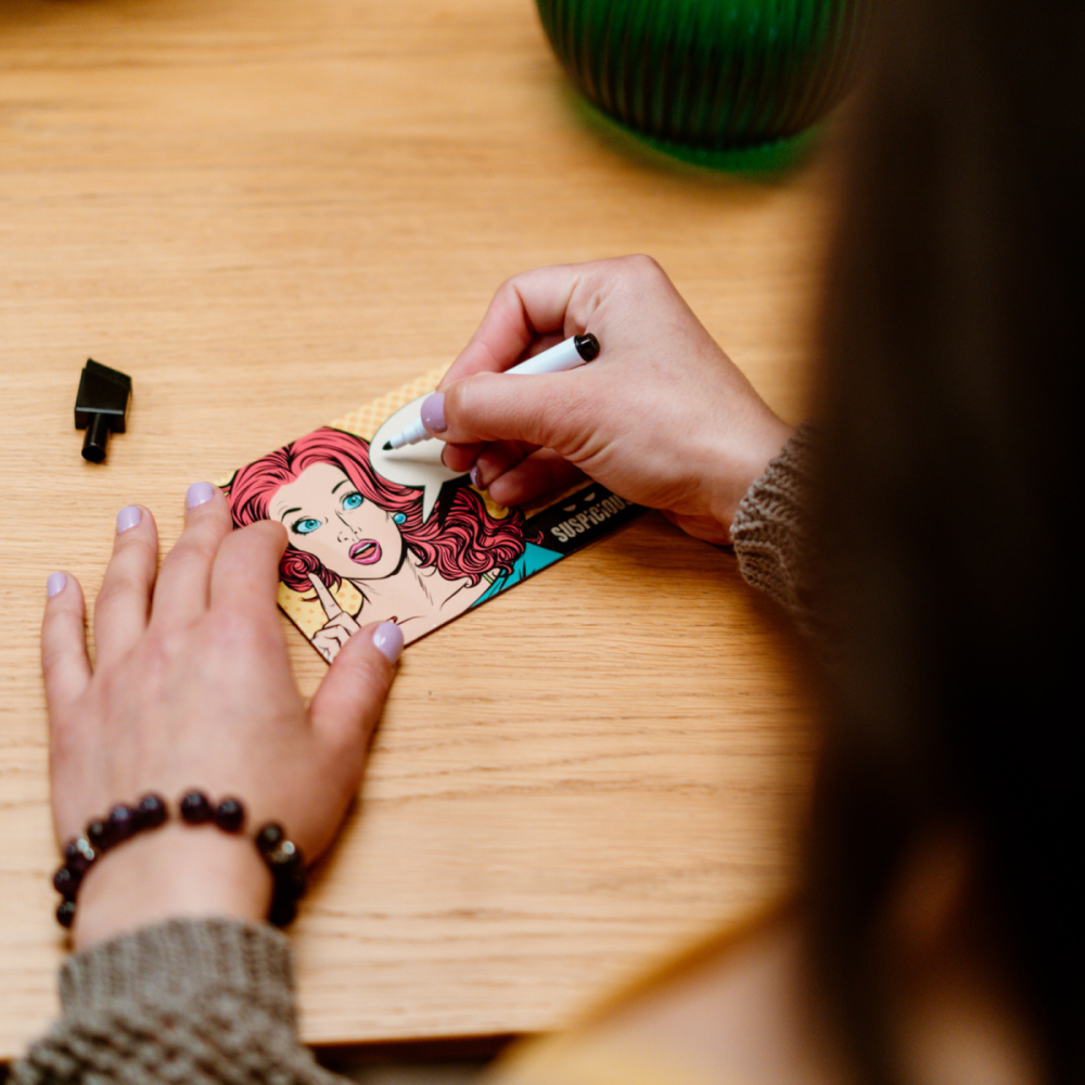 Mains d'une personne écrivant sur une carte avec une illustration pop art.