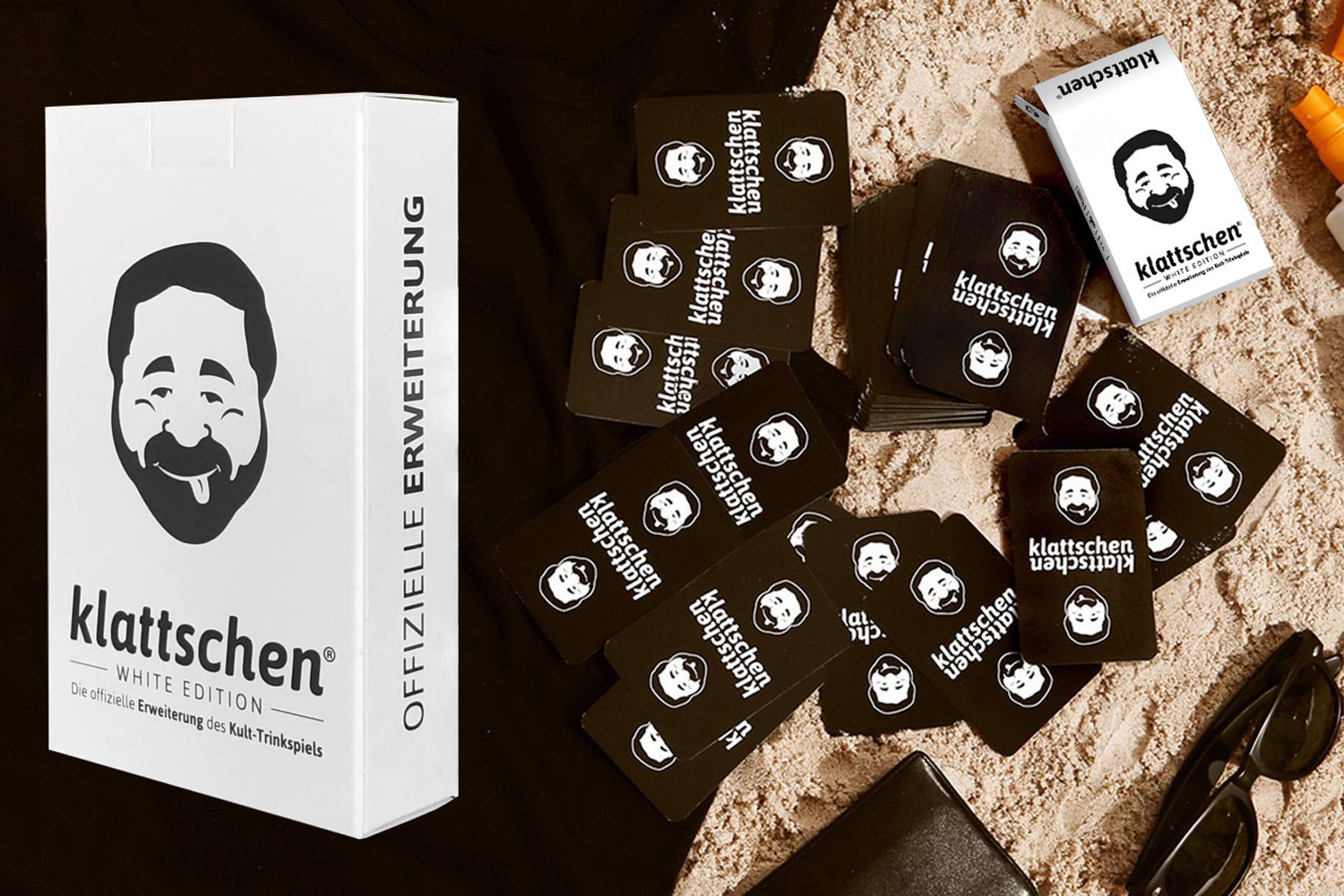 Karten auf Sand verstreut, eine weiße Box mit einem Cartoon-Gesicht und eine Sonnenbrille. Die Karten haben das gleiche Gesicht.