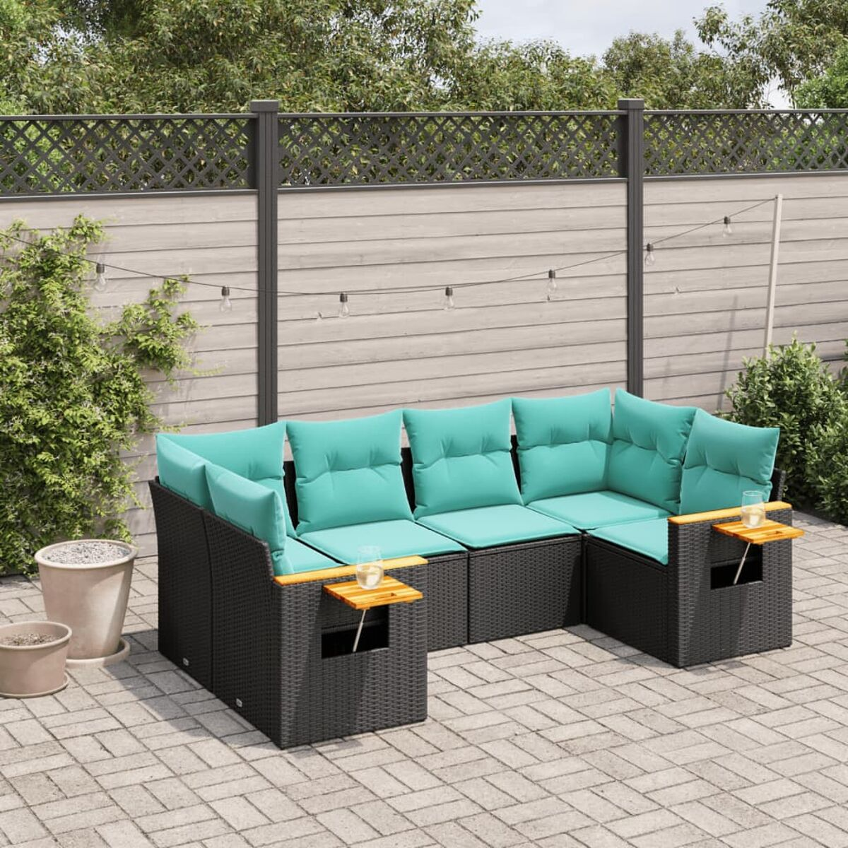 Ein schwarzes Outdoor-Sofa aus Korbgeflecht mit türkisfarbenen Kissen, auf einer Terrasse mit Zaun.