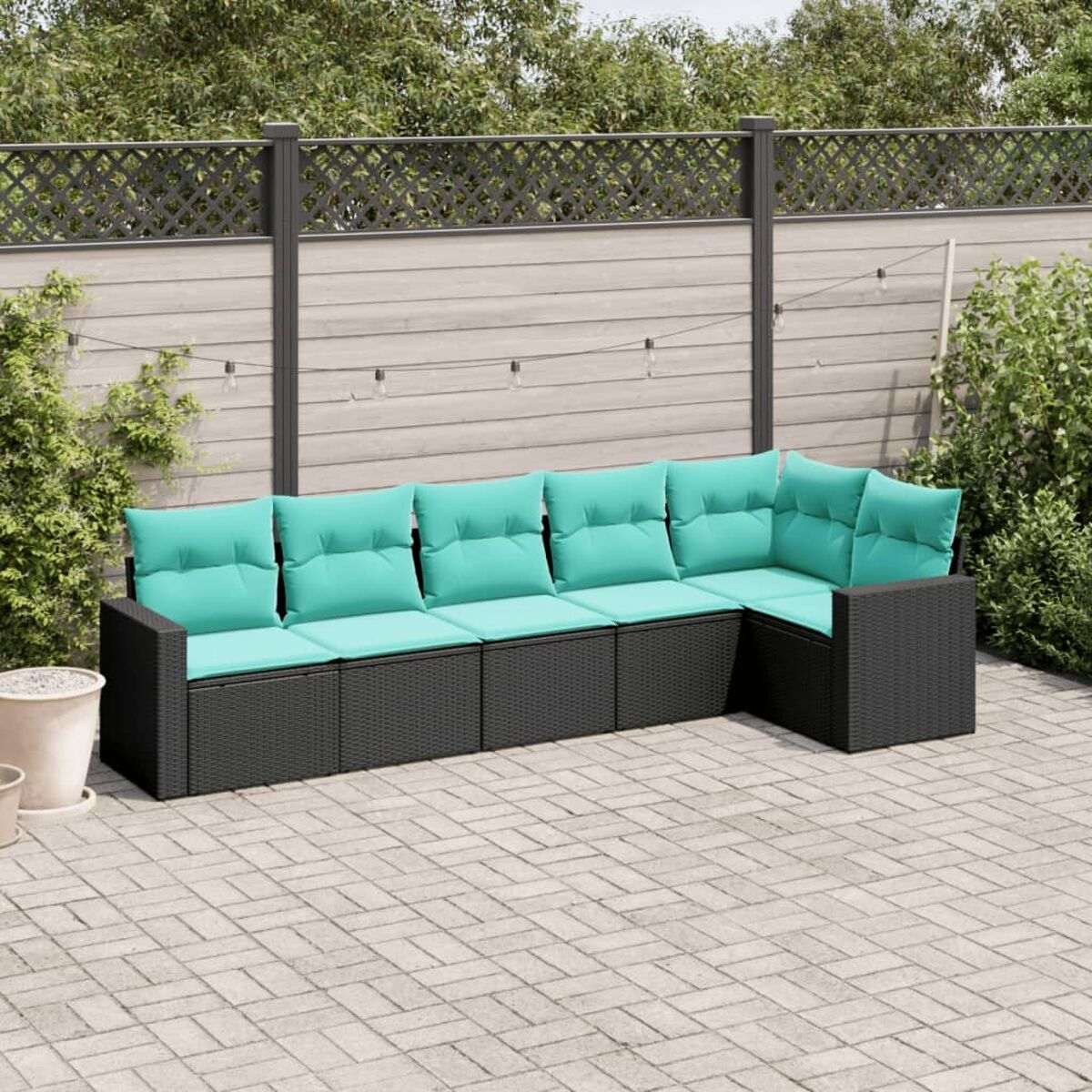 Juego de muebles de mimbre negro para exteriores con cojines turquesa, en patio de ladrillos, plantas y valla.