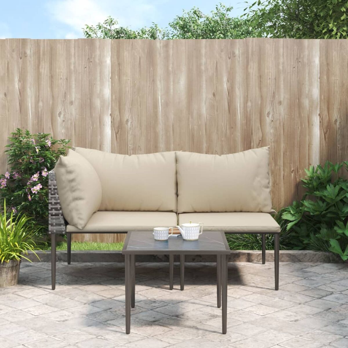 Set di sedute per esterni con cuscini beige e tavolino su un patio, sfondo di recinzione in legno.