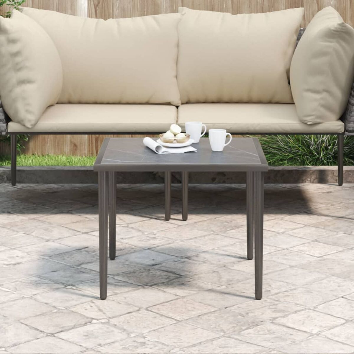 Outdoor-Sitzbereich mit Sofa und Tisch. Weiße Kissen. Kaffeetassen und Snacks auf dem Tisch.