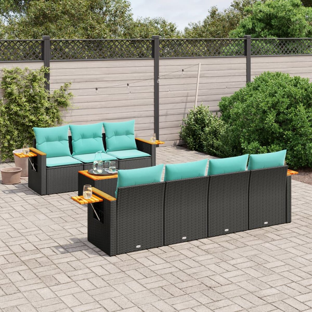 Terrasseneinrichtung mit schwarzem Korbsessel und türkisfarbenen Kissen, mit Ziegelpflaster und Zaun.