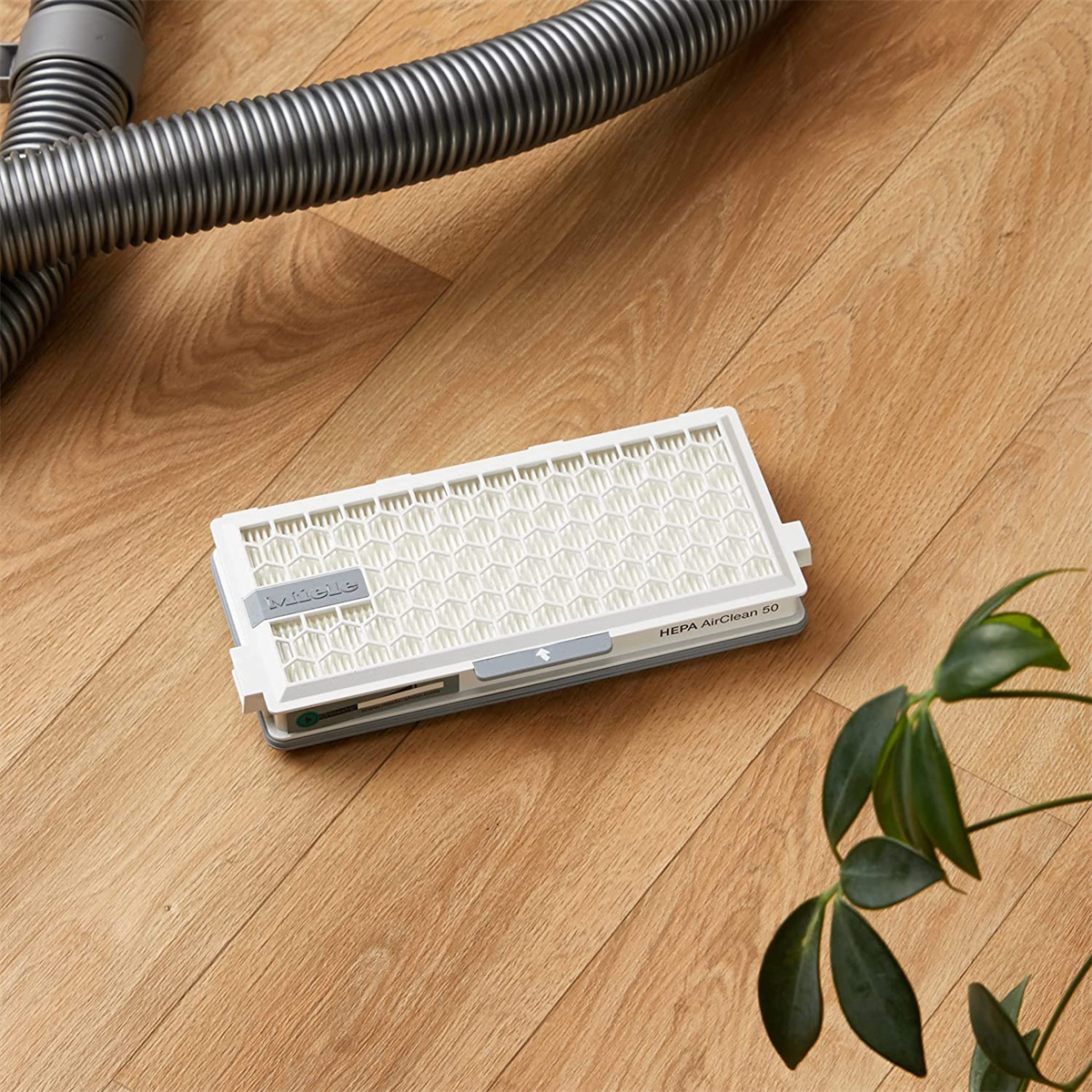 Ein weißer HEPA AirClean 50 Filter für einen Staubsauger, mit einem Staubsaugerschlauch und Holzboden.