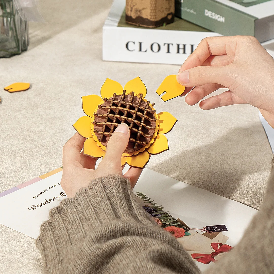 Een persoon die een houten zonnebloempuzzel in elkaar zet. De stukken zijn geel en bruin.