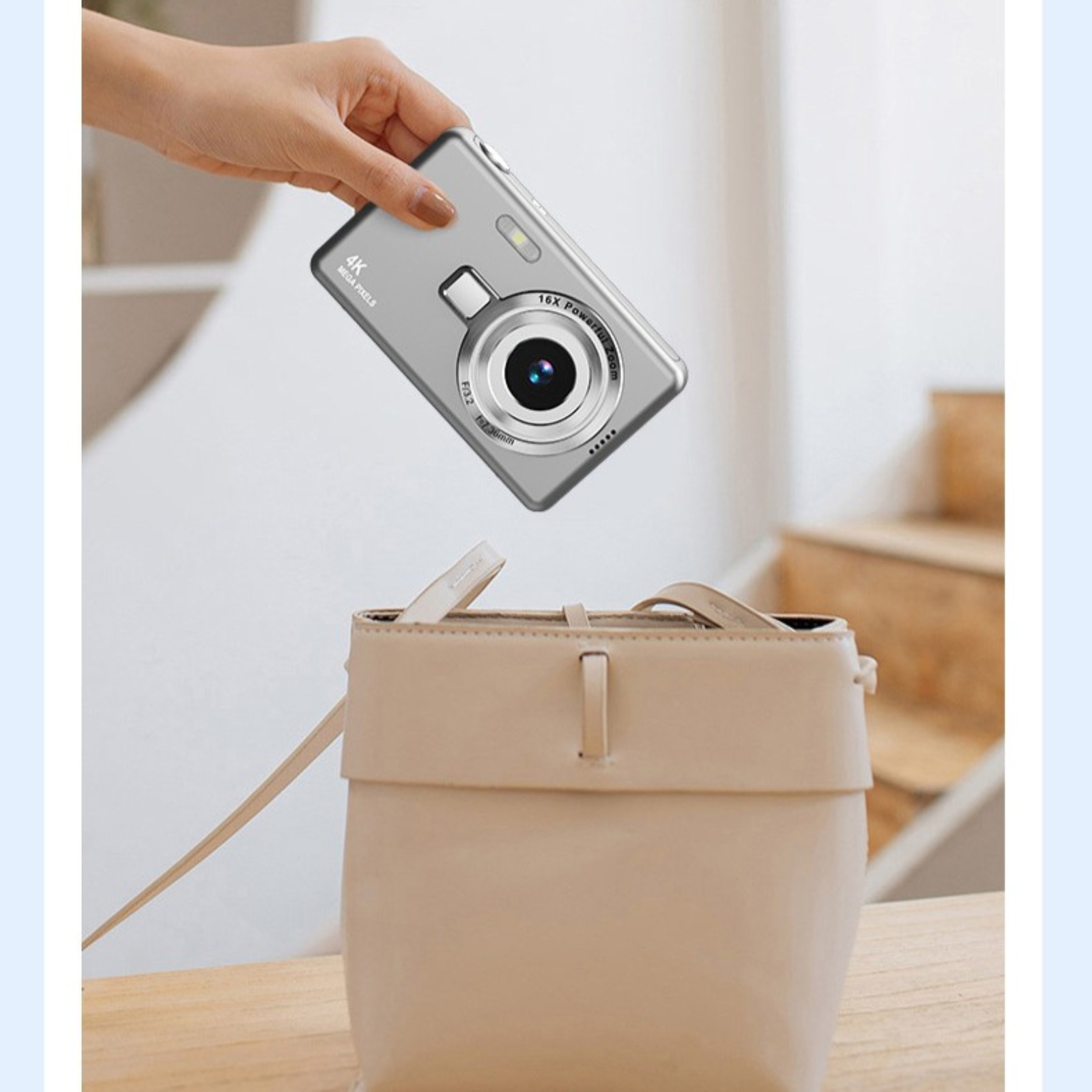 Silberne Digitalkamera wird von einer Hand in eine beige Handtasche gelegt.