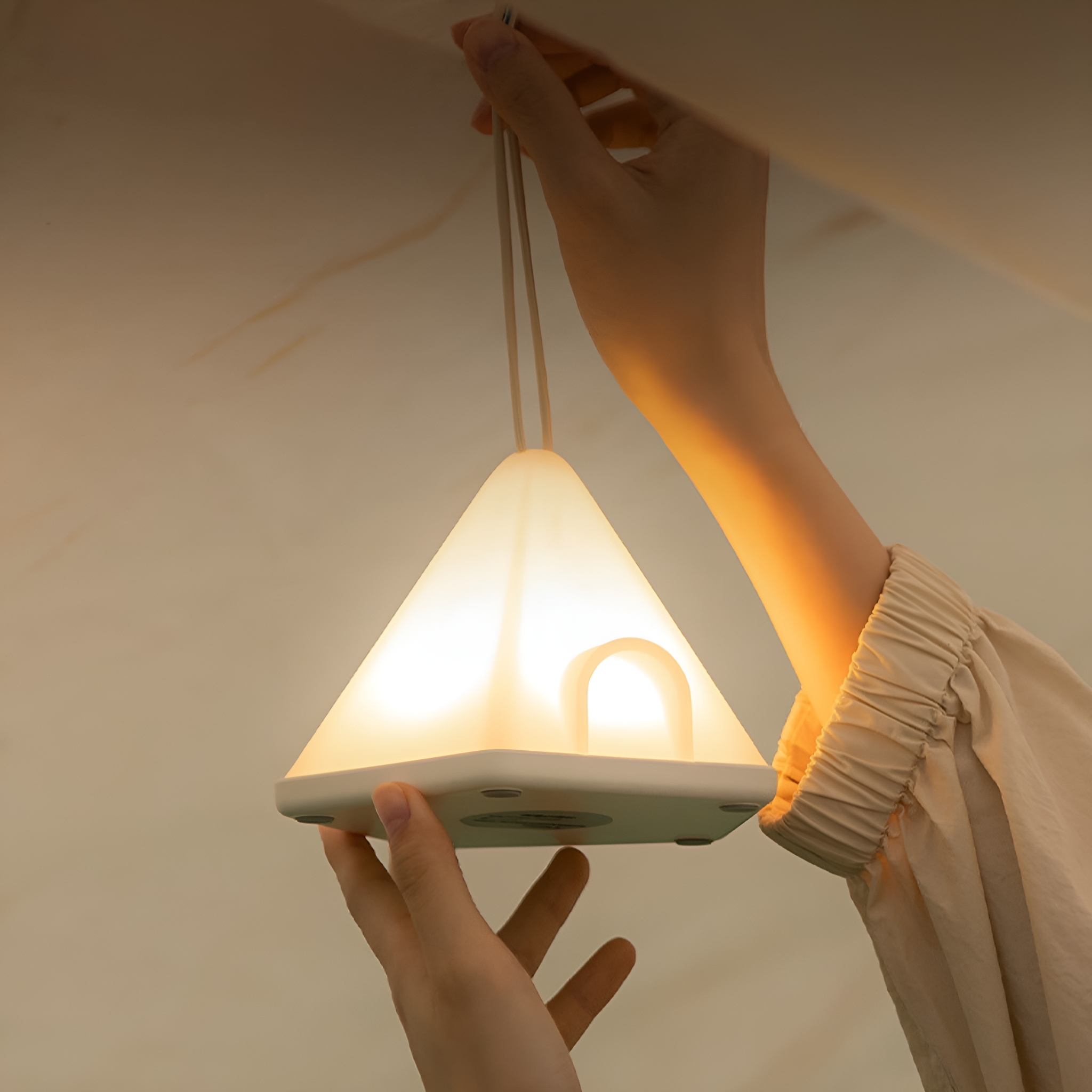 Eine Person hält eine leuchtende, weiße dreieckige Lampe mit Griff. Gedämpfte Beleuchtung.