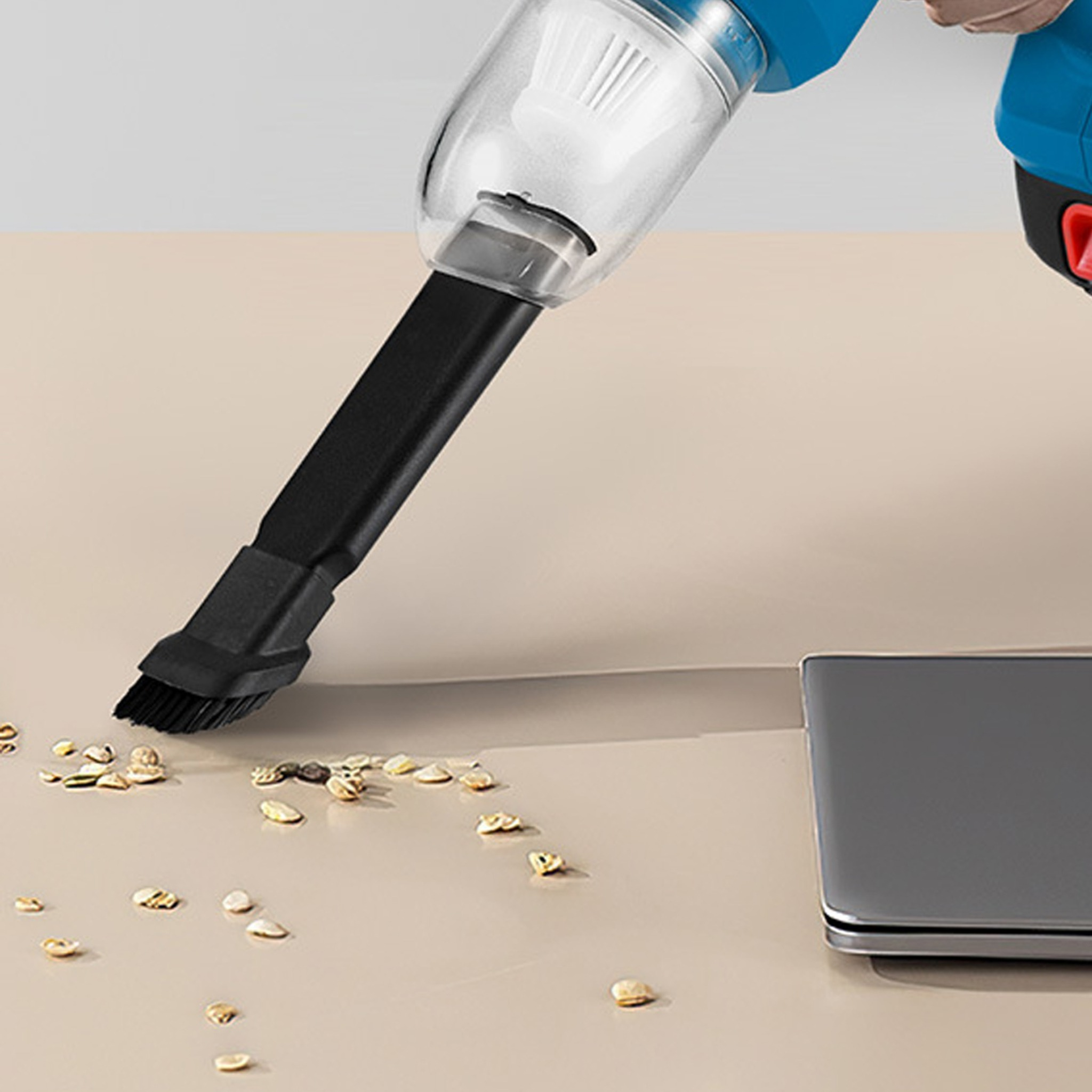 Ein Staubsauger, der Krümel von einer beigefarbenen Oberfläche in der Nähe eines Laptops absaugt.