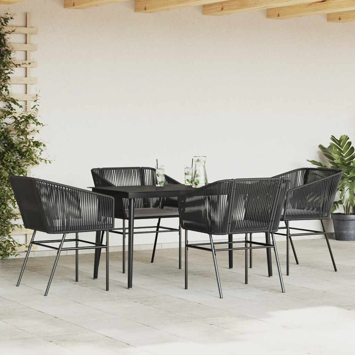 Set da pranzo all'aperto: tavolo e sedie neri su un ponte di legno, con piante e parete bianca.
