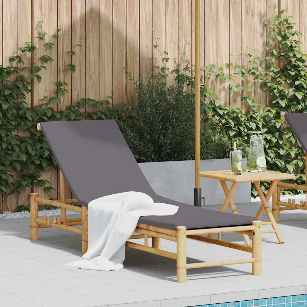 Una chaise longue grigia con un asciugamano bianco accanto a un tavolino e a un ombrellone vicino a una piscina.