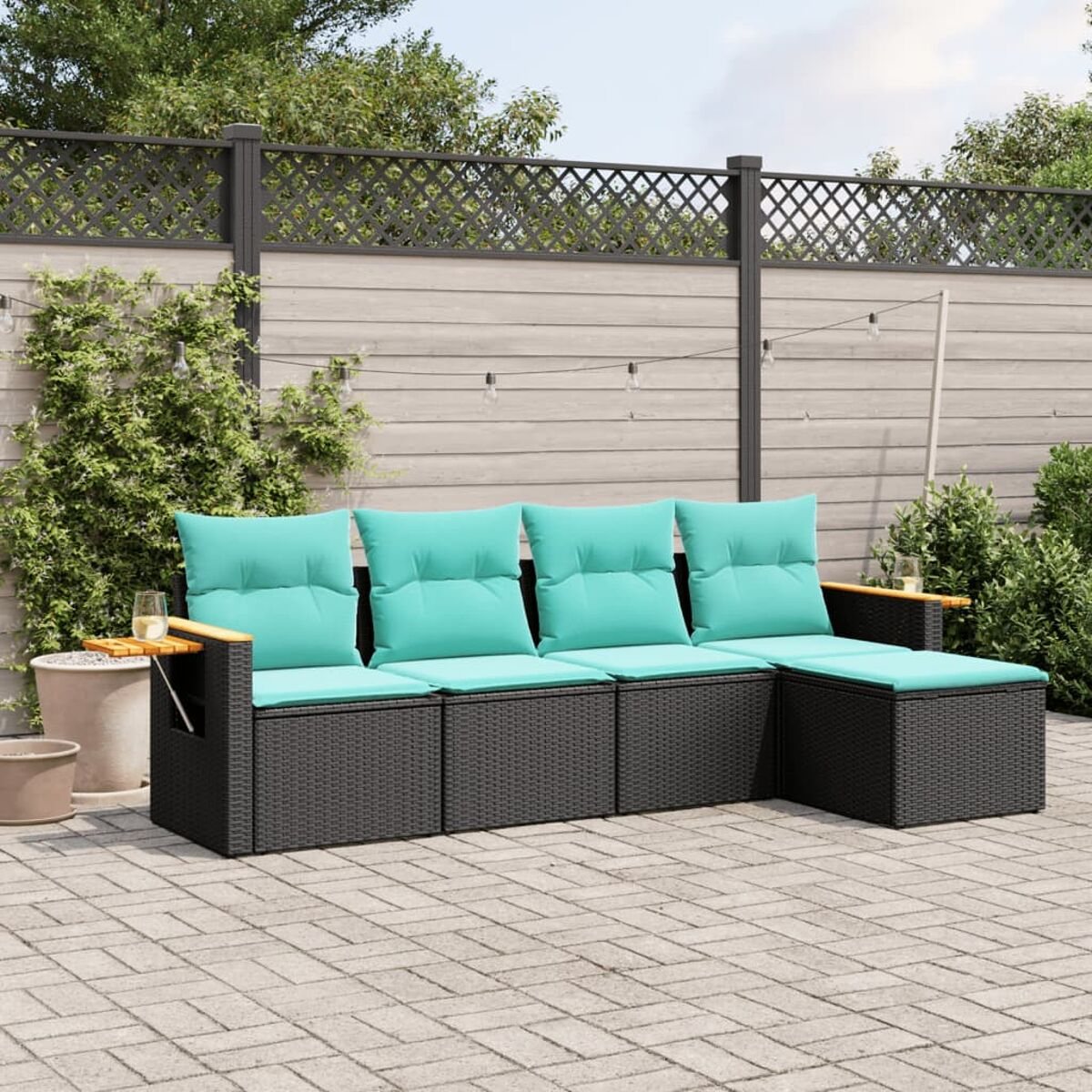 Set divano in vimini nero per esterni con cuscini turchese. Il set è su un patio in mattoni con una recinzione in legno sullo sfondo.