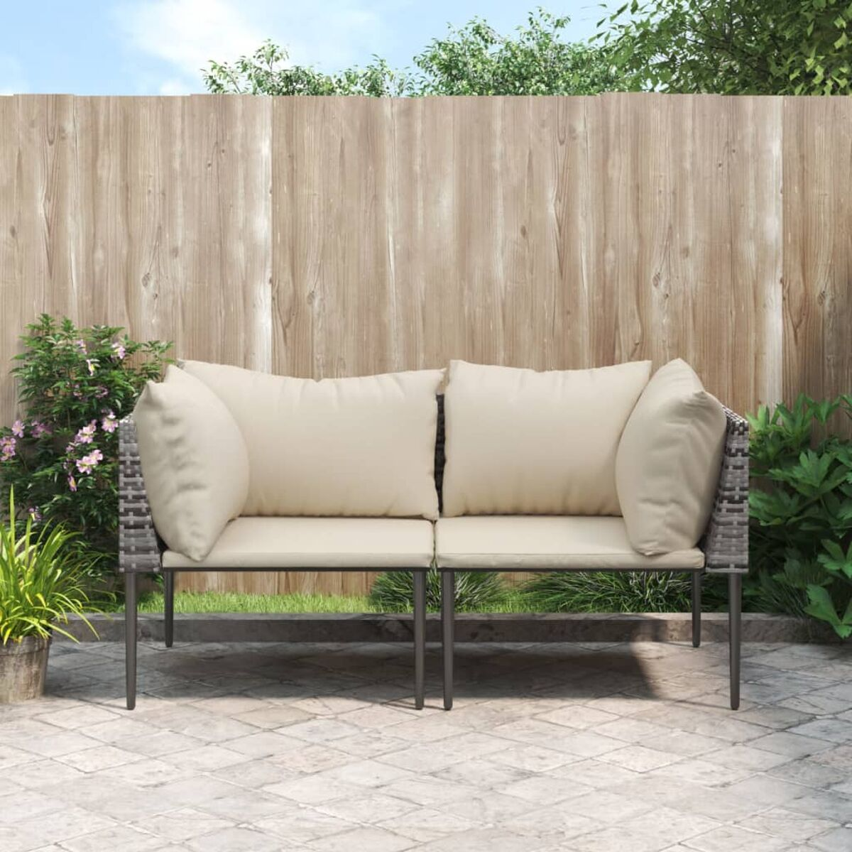 Divano da patio esterno con due cuscini. Struttura grigia, cuscini beige e sfondo di una recinzione in legno.
