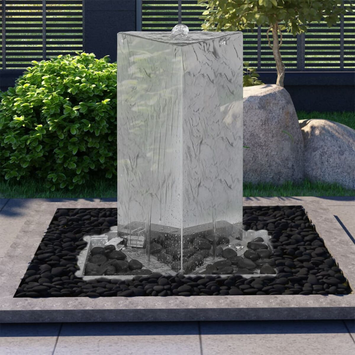Ein hoher, klarer Glasbrunnen mit Wasserfluss von oben, eingebettet in schwarze Steine.