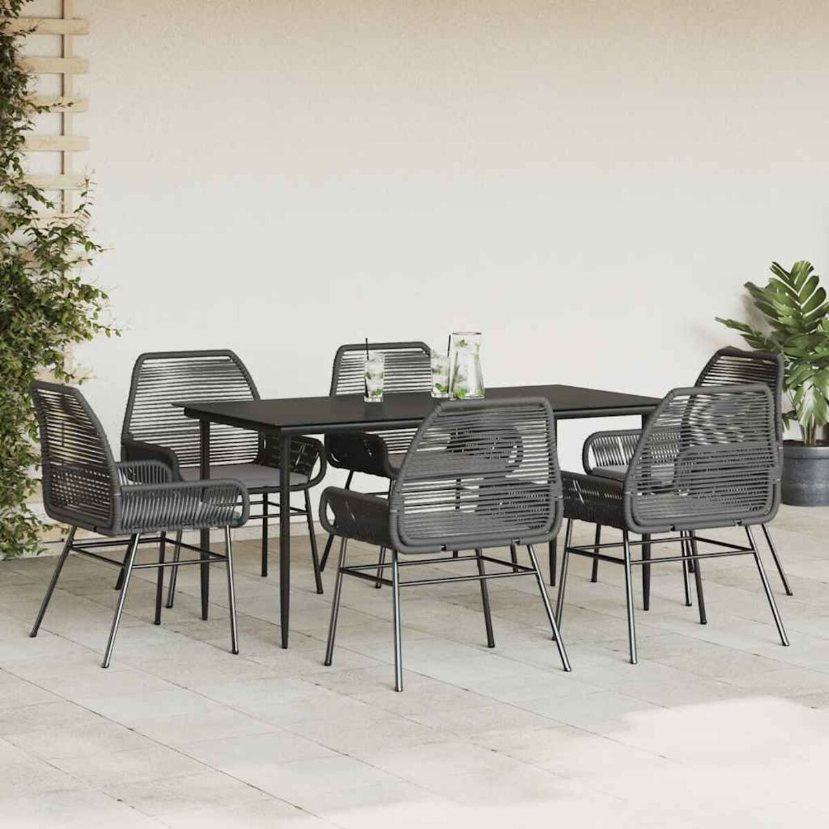 Set da pranzo all'aperto con tavolo nero e sei sedie grigie intrecciate. Parete bianca sullo sfondo.
