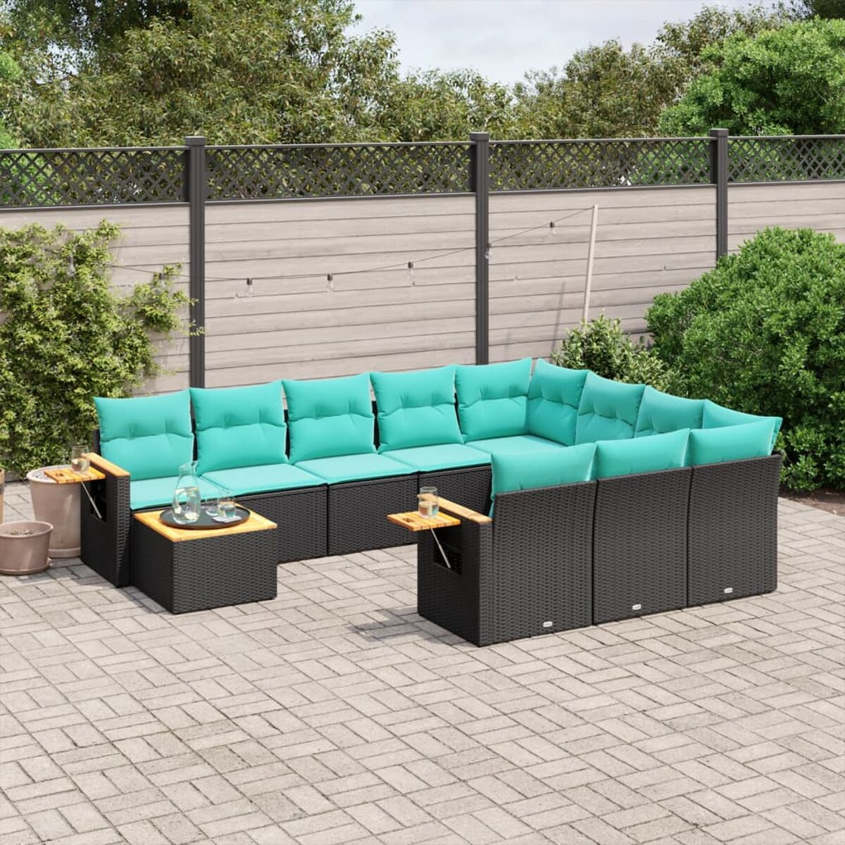 Un divano componibile in vimini nero per esterni con cuscini verde acqua, due tavolini e un patio in mattoni.
