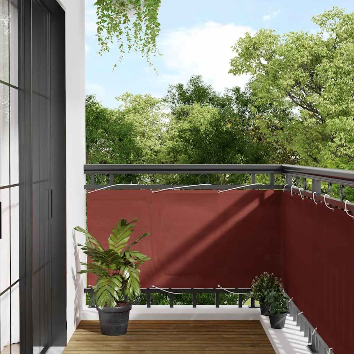 Balcone con piante, uno schermo per la privacy rosso e vista sugli alberi.