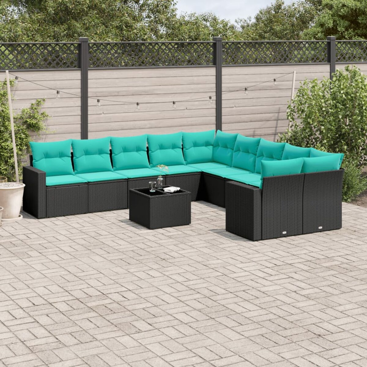 Set divano da esterno in vimini nero con cuscini turchese, tavolo e patio in mattoni con recinzione sullo sfondo.