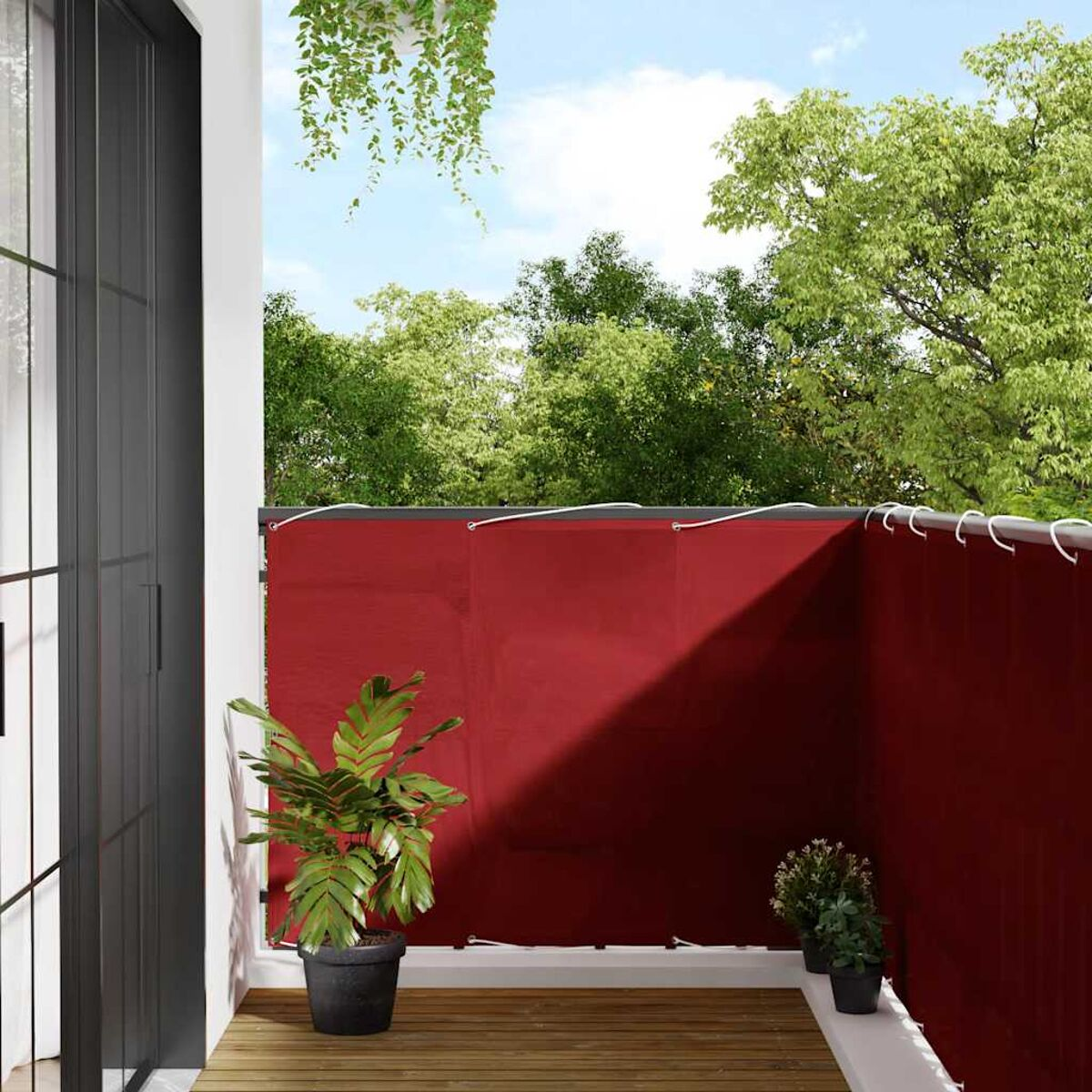 Un balcone con uno schermo rosso, piante e una vista di alberi e cielo.