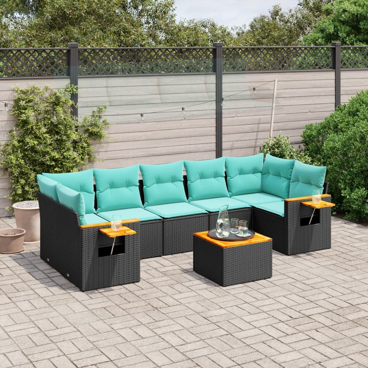 Set divano in rattan nero da esterno con cuscini turchese, tavolino e patio in mattoni.