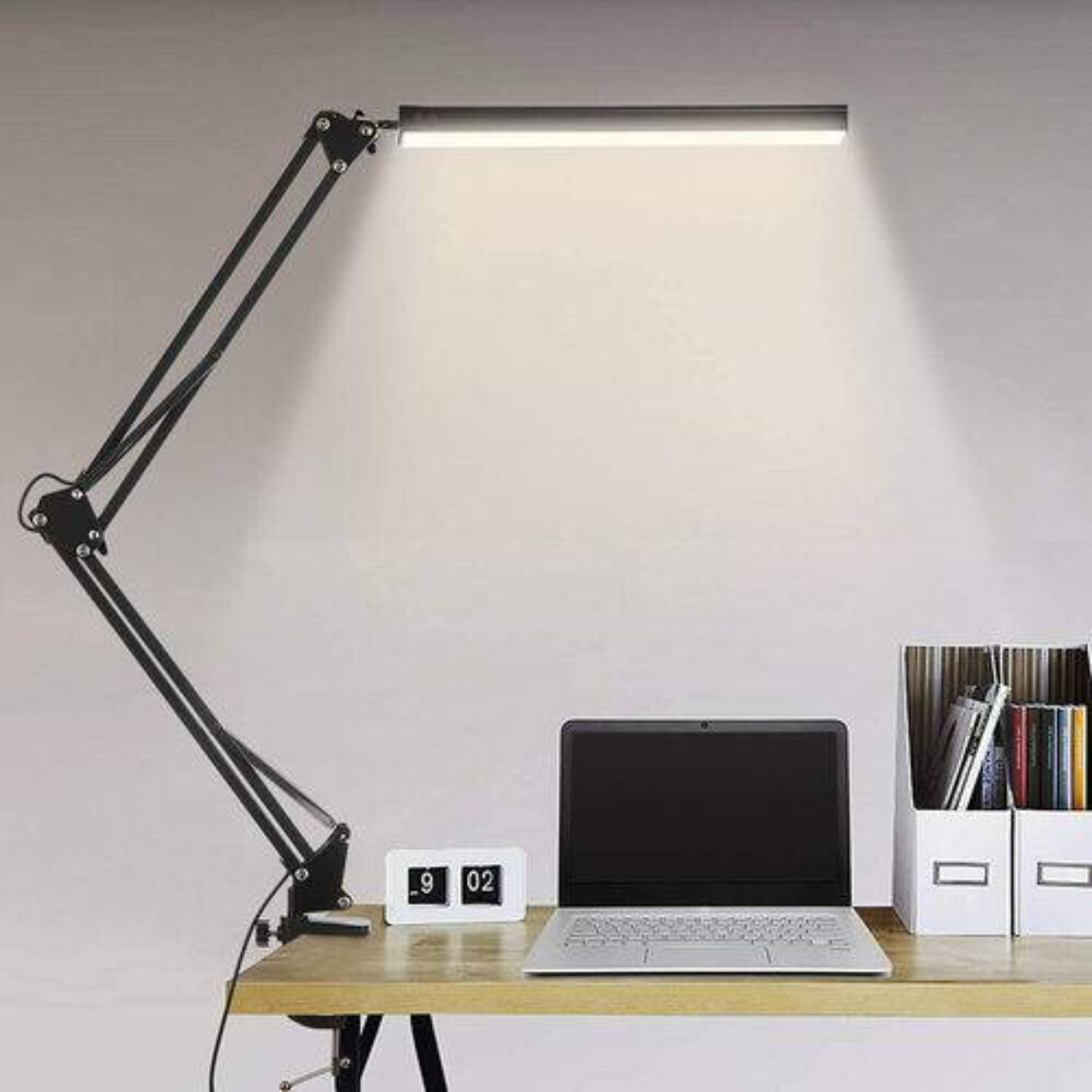 Schwarze Schreibtischlampe über einem Schreibtisch mit Laptop, Uhr und Akten.