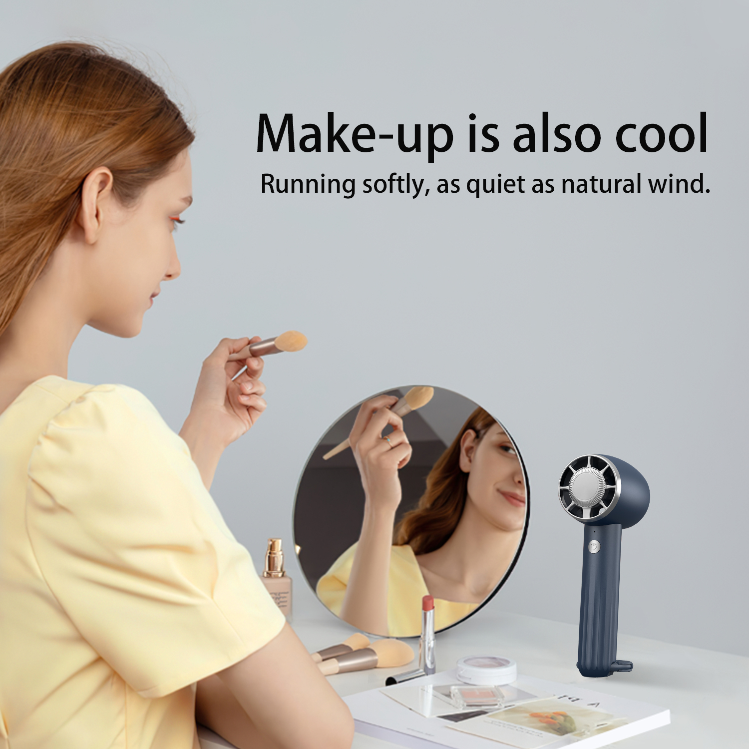 Woman applying makeup using a mirror, with a small fan. Text says "Make-up is also cool".