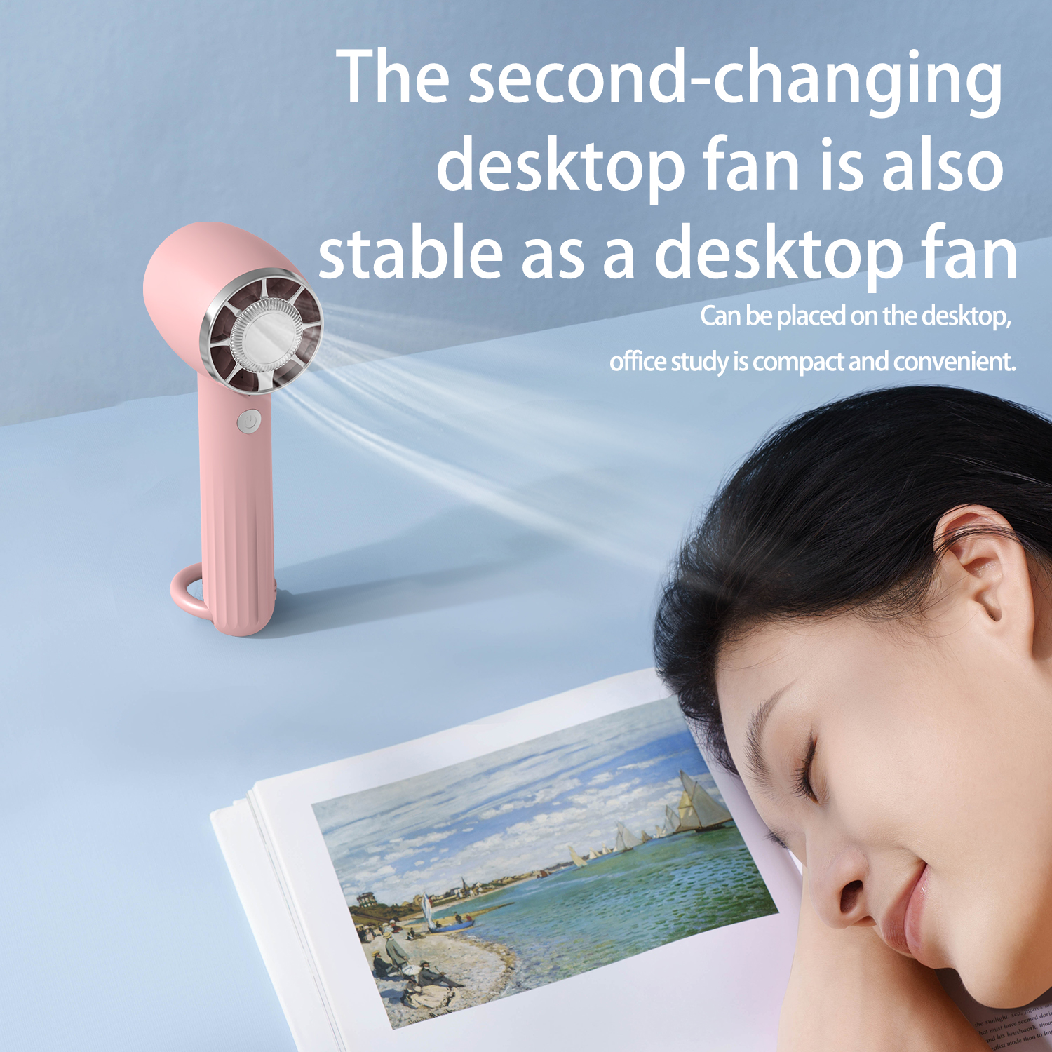 Pink desktop fan with a woman sleeping next to a book with a painting on the page.