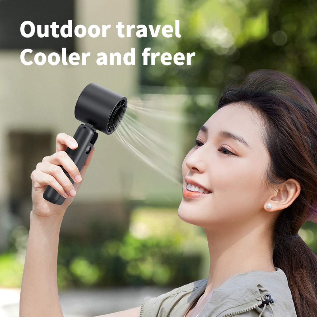A woman uses a black handheld fan. She smiles as the fan blows air towards her face.