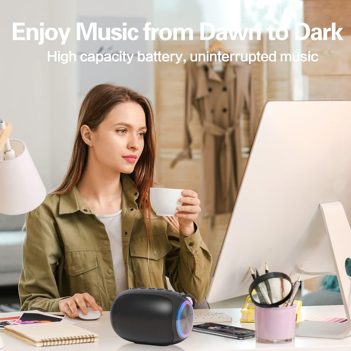 Frau am Schreibtisch mit Maus, hört Musik von einem schwarzen Lautsprecher, hält eine Tasse.